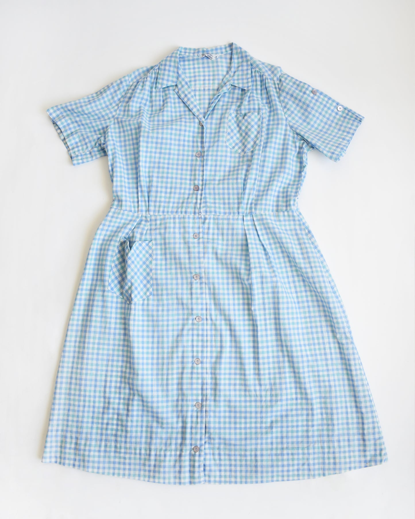 a flat lay of a vintage 1950s light blue and white gingham short-sleeve button-front dress displayed on a mannequin against a plain white background.