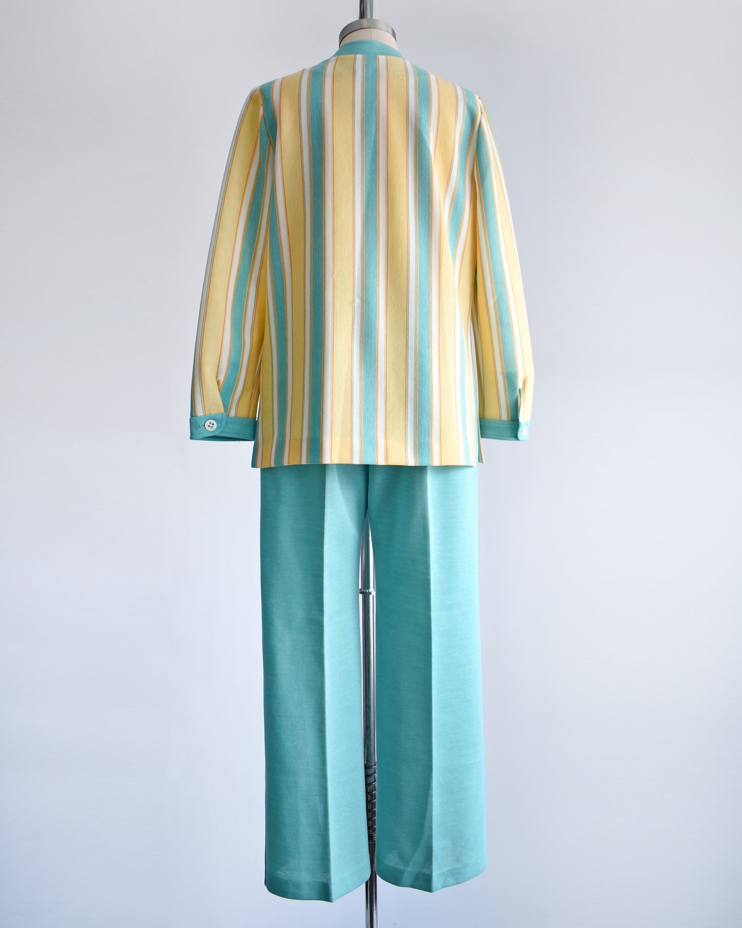 back view of a vintage 1970s two piece pantsuit. The top is yellow, blue, white and orange striped, and the pants are the same matching blue.