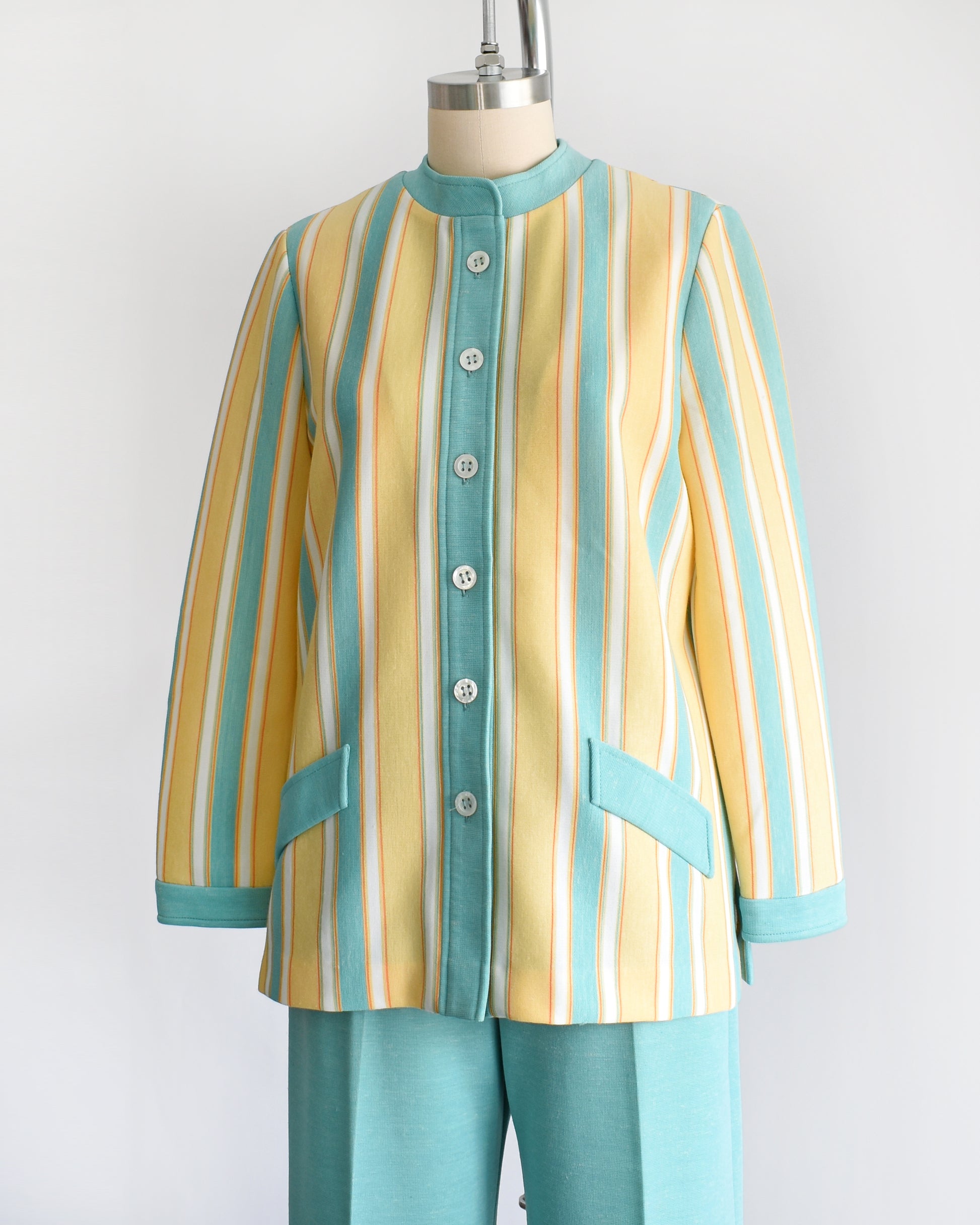 side front view of a vintage 1970s two piece pantsuit. The top is yellow, blue, white and orange striped, and the pants are the same matching blue.