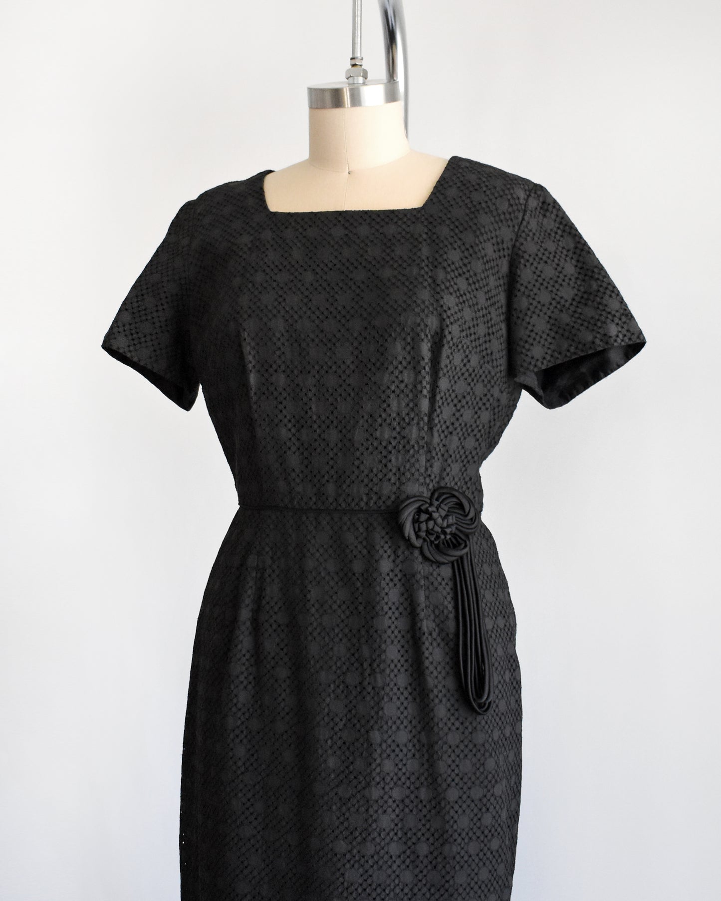 side font view of a vintage 1960s black eyelet dress on a mannequin on a dress form