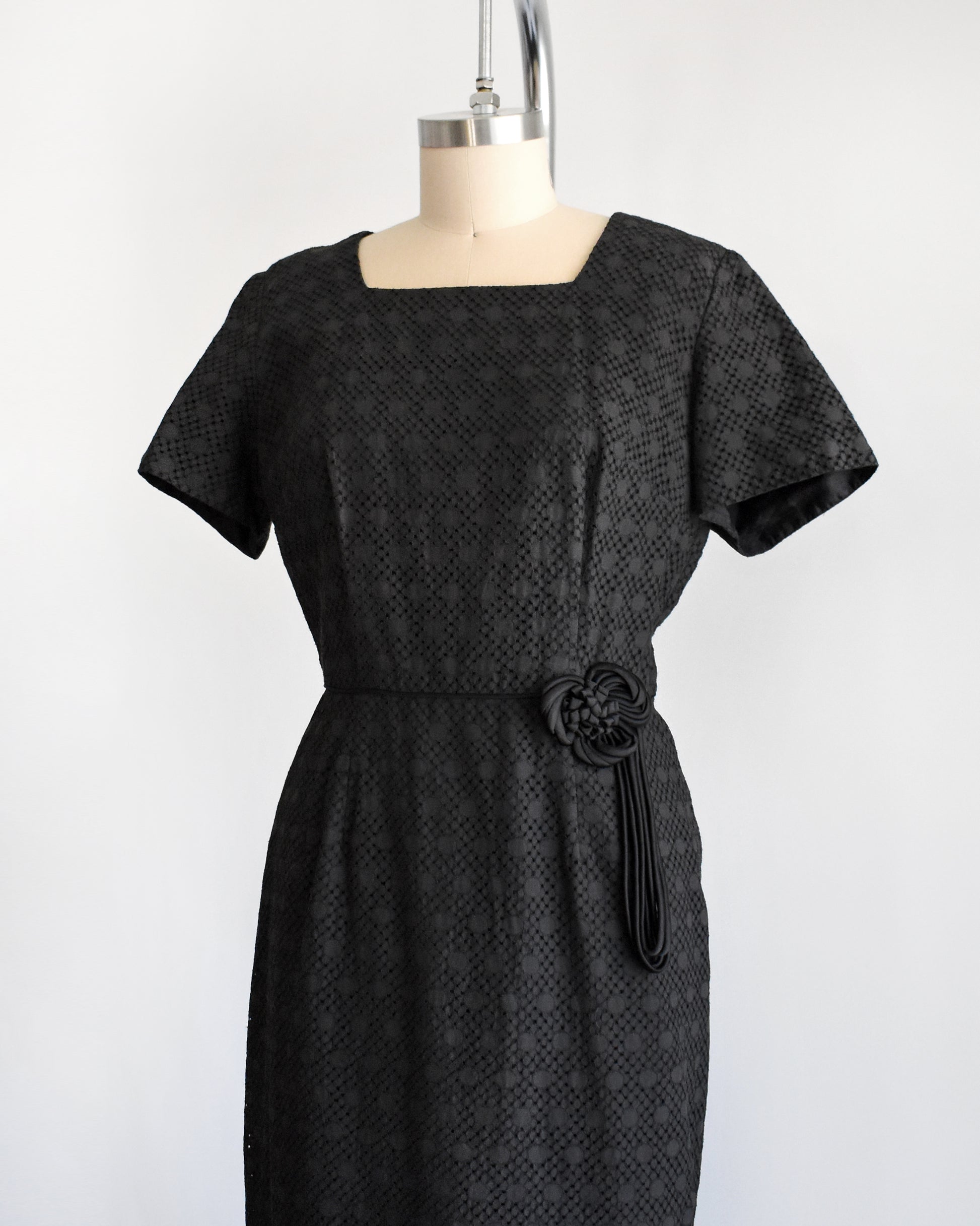 side font view of a vintage 1960s black eyelet dress on a mannequin on a dress form