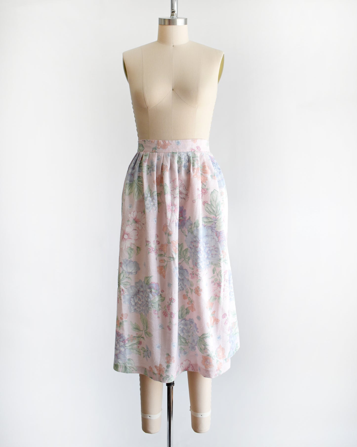 A vintage 1980s  high-waisted midi skirt with a pastel floral print, displayed on a beige dress form mannequin against a plain white background.