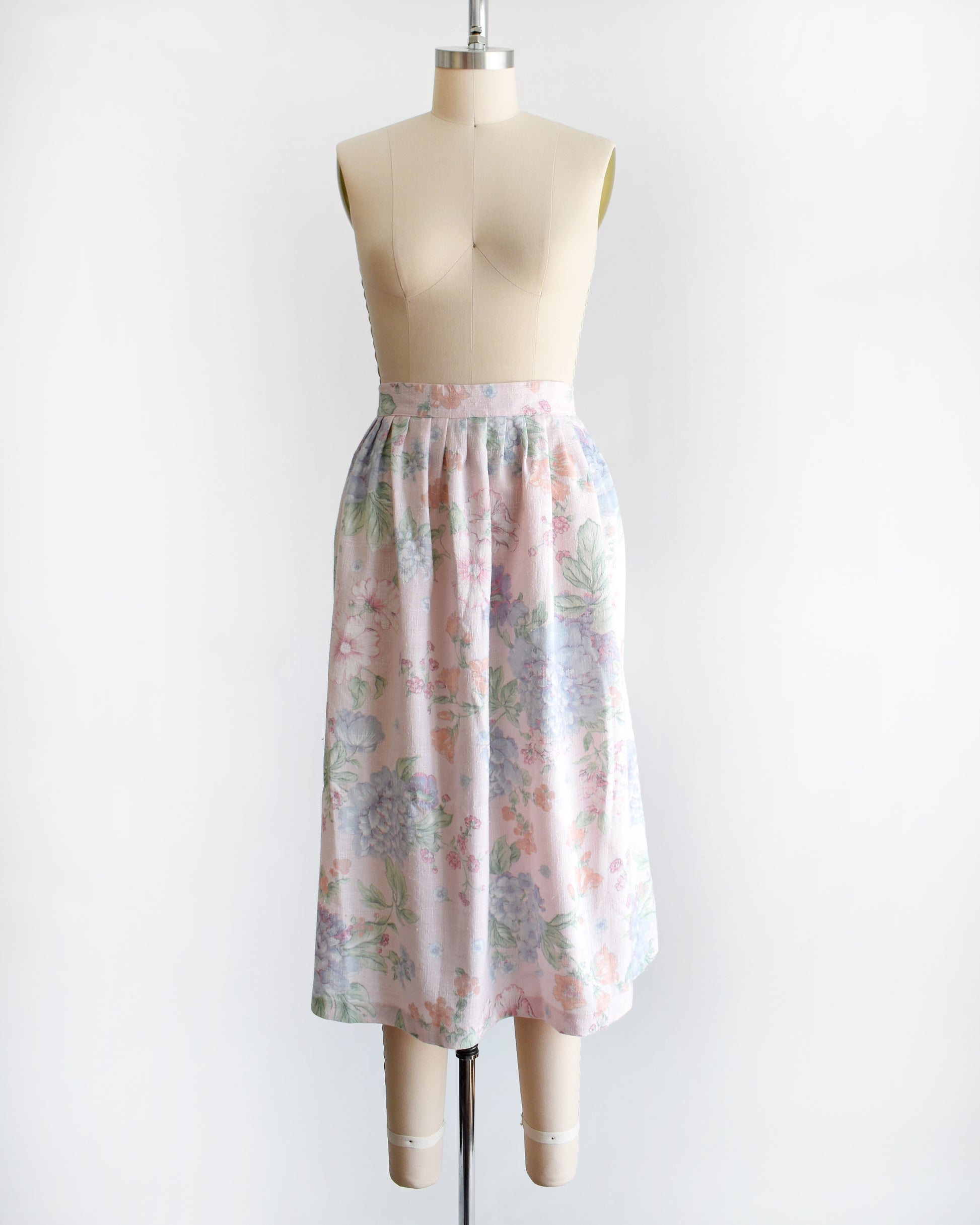 A vintage 1980s  high-waisted midi skirt with a pastel floral print, displayed on a beige dress form mannequin against a plain white background.