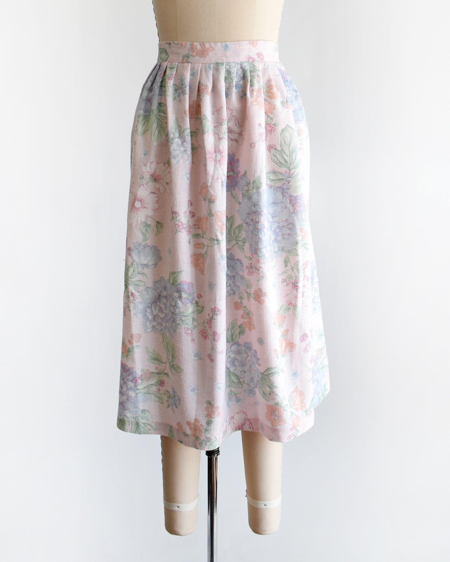 A vintage 1980s  high-waisted midi skirt with a pastel floral print, displayed on a beige dress form mannequin against a plain white background.