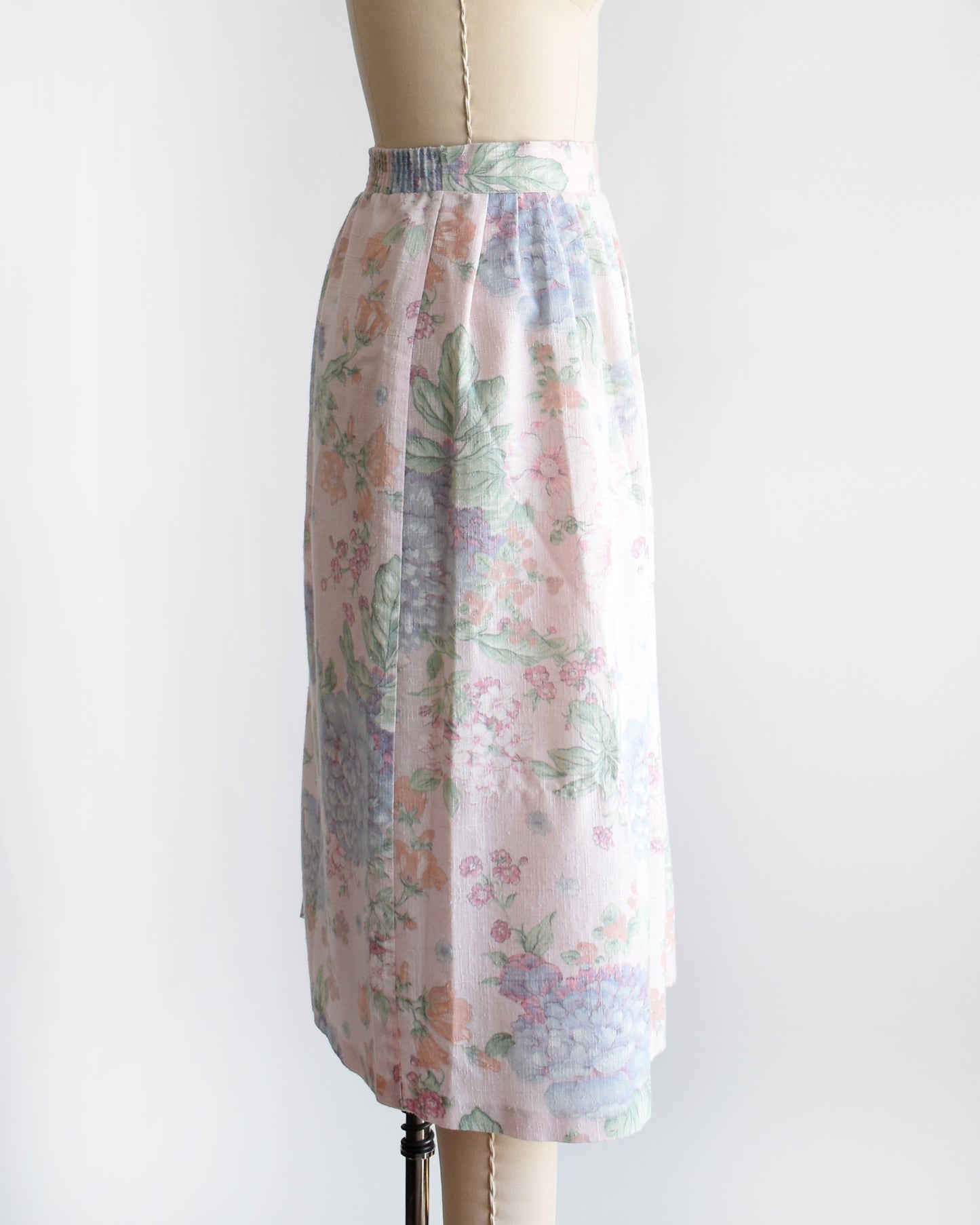 side view of a vintage 1980s  high-waisted midi skirt with a pastel floral print, displayed on a beige dress form mannequin against a plain white background.