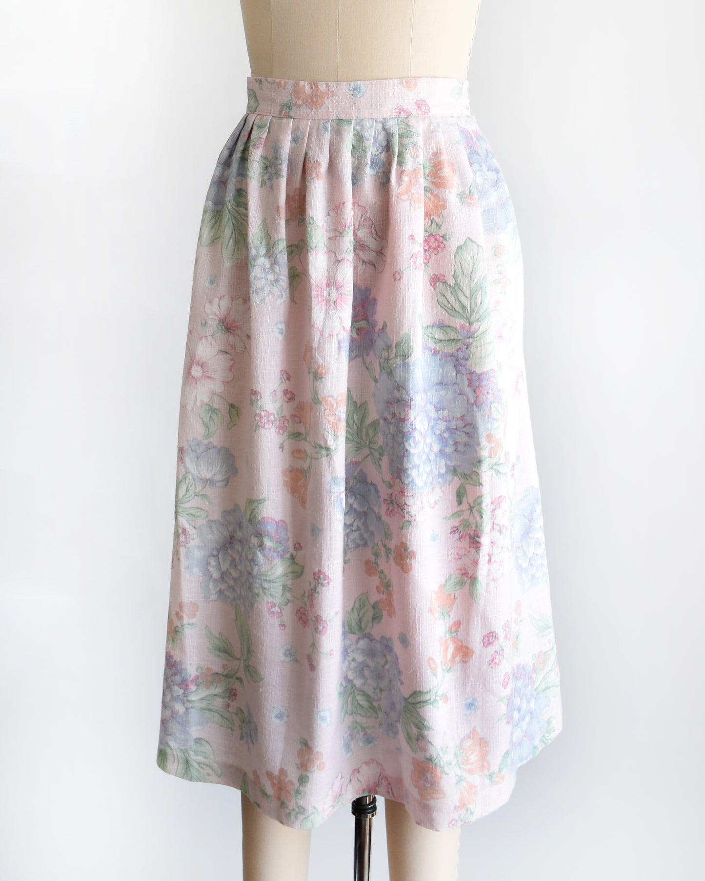 side front view of a vintage 1980s  high-waisted midi skirt with a pastel floral print, displayed on a beige dress form mannequin against a plain white background.