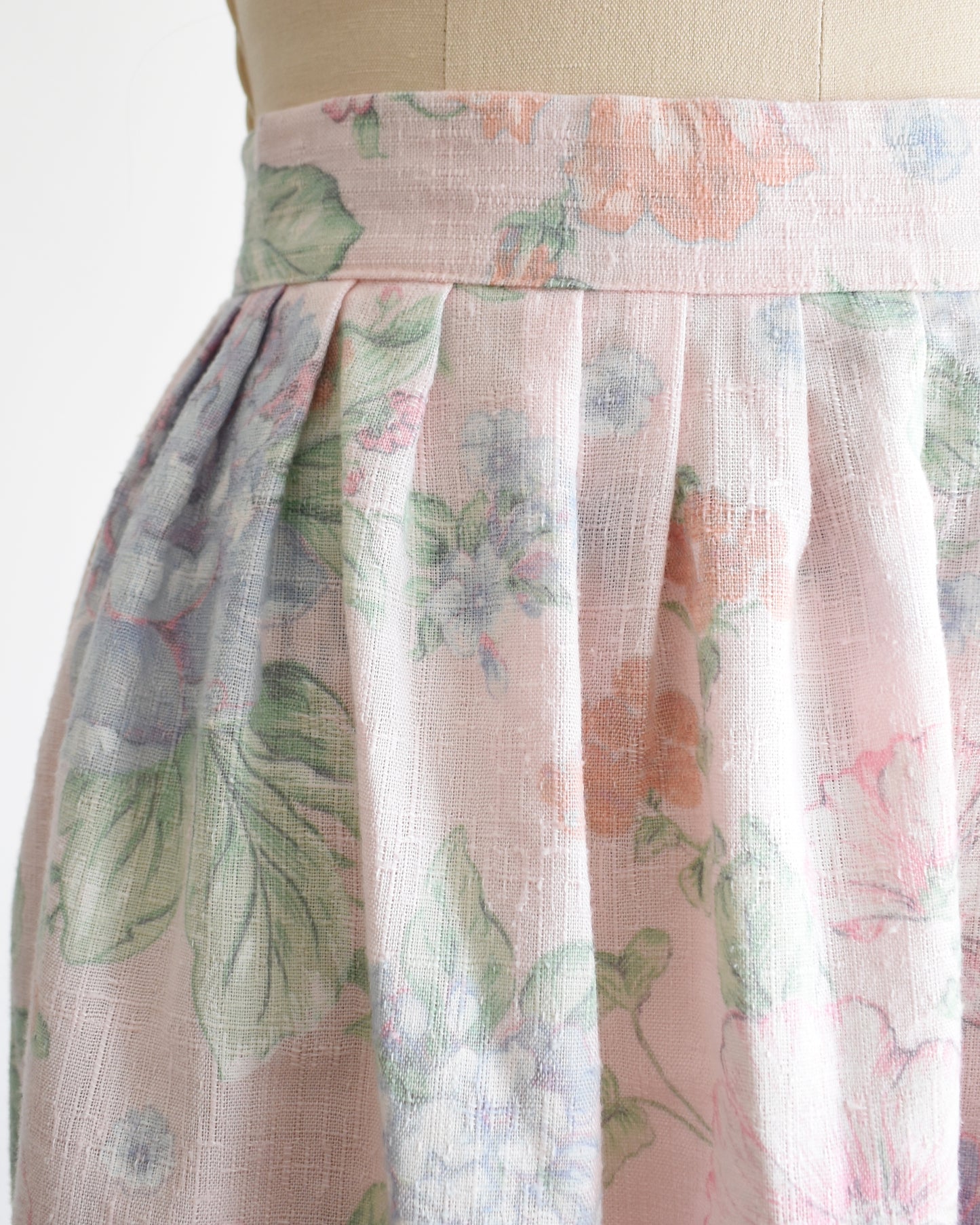 close up of the waist of a vintage 1980s  high-waisted midi skirt with a pastel floral print, displayed on a beige dress form mannequin against a plain white background.