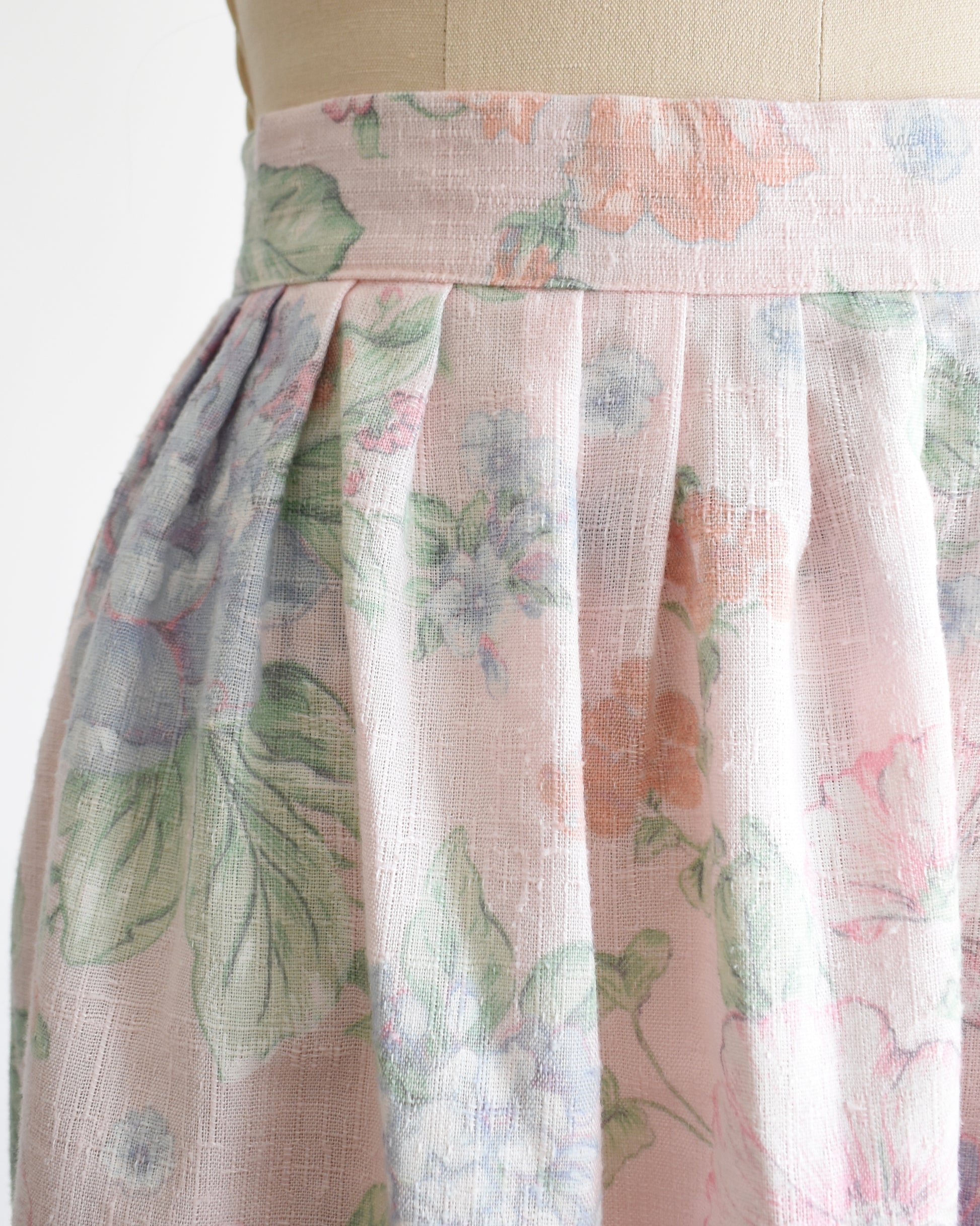 close up of the waist of a vintage 1980s  high-waisted midi skirt with a pastel floral print, displayed on a beige dress form mannequin against a plain white background.