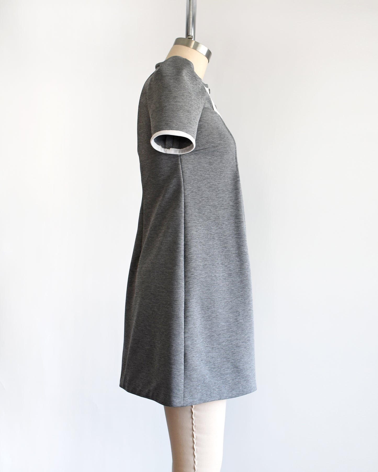 side view of a vintage 1960s gray dress with white collar on a mannequin against a white background