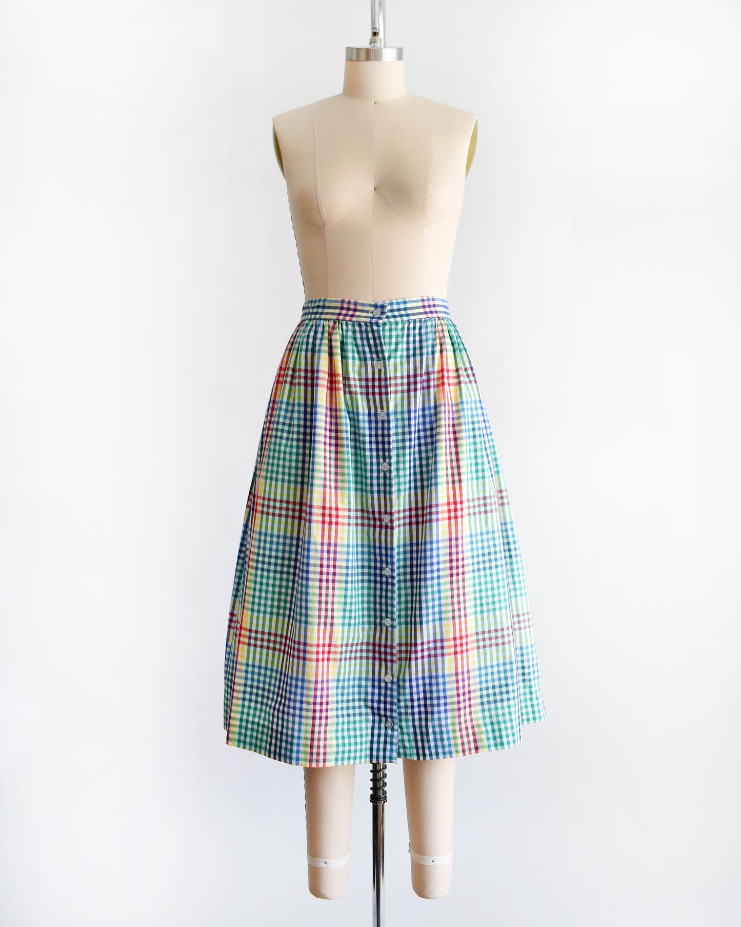 a vintage 1980s multicolor plaid midi skirt displayed on a beige dress form mannequin against a plain white background.
