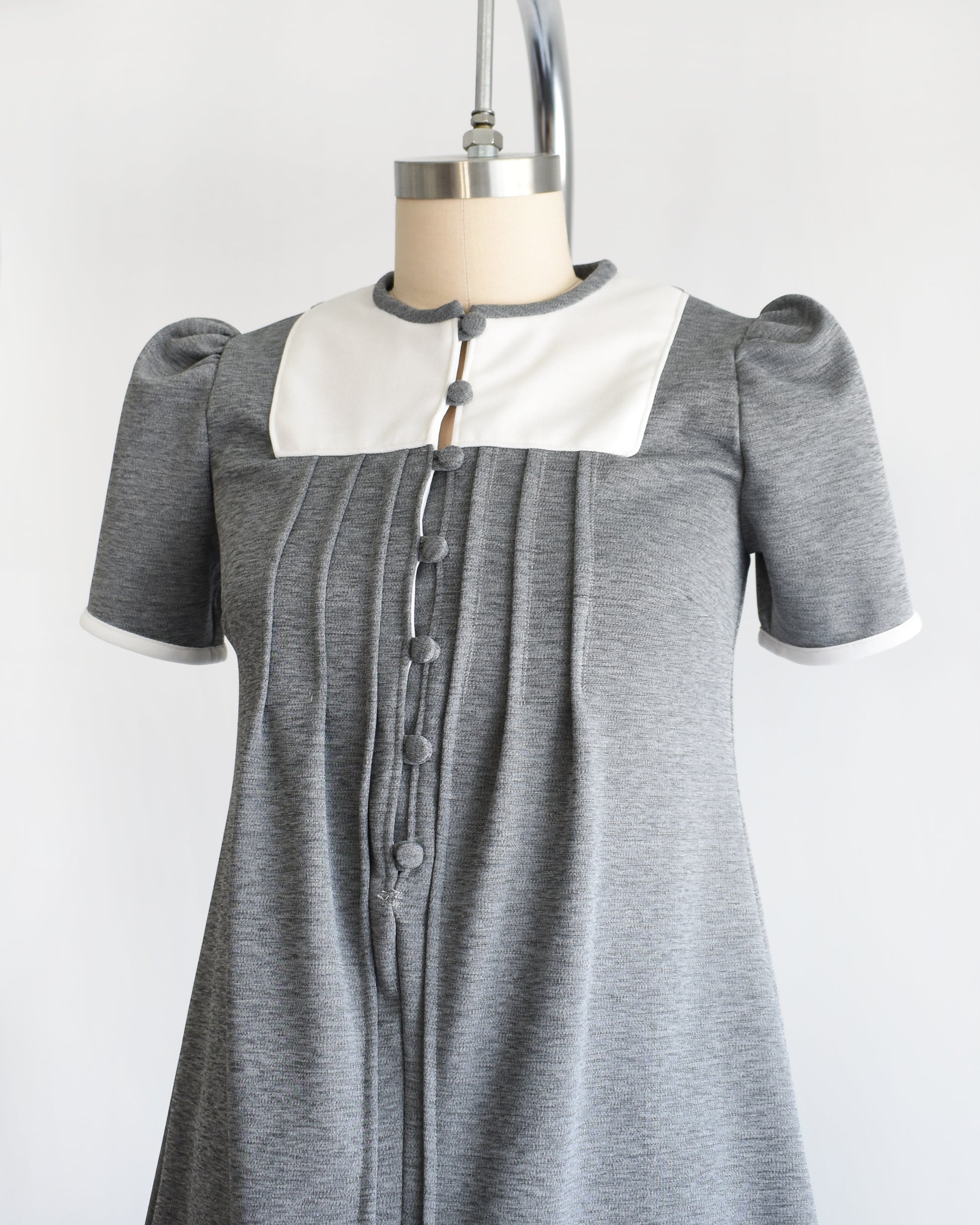 side front view of a vintage 1960s gray dress with white collar on a mannequin against a white background