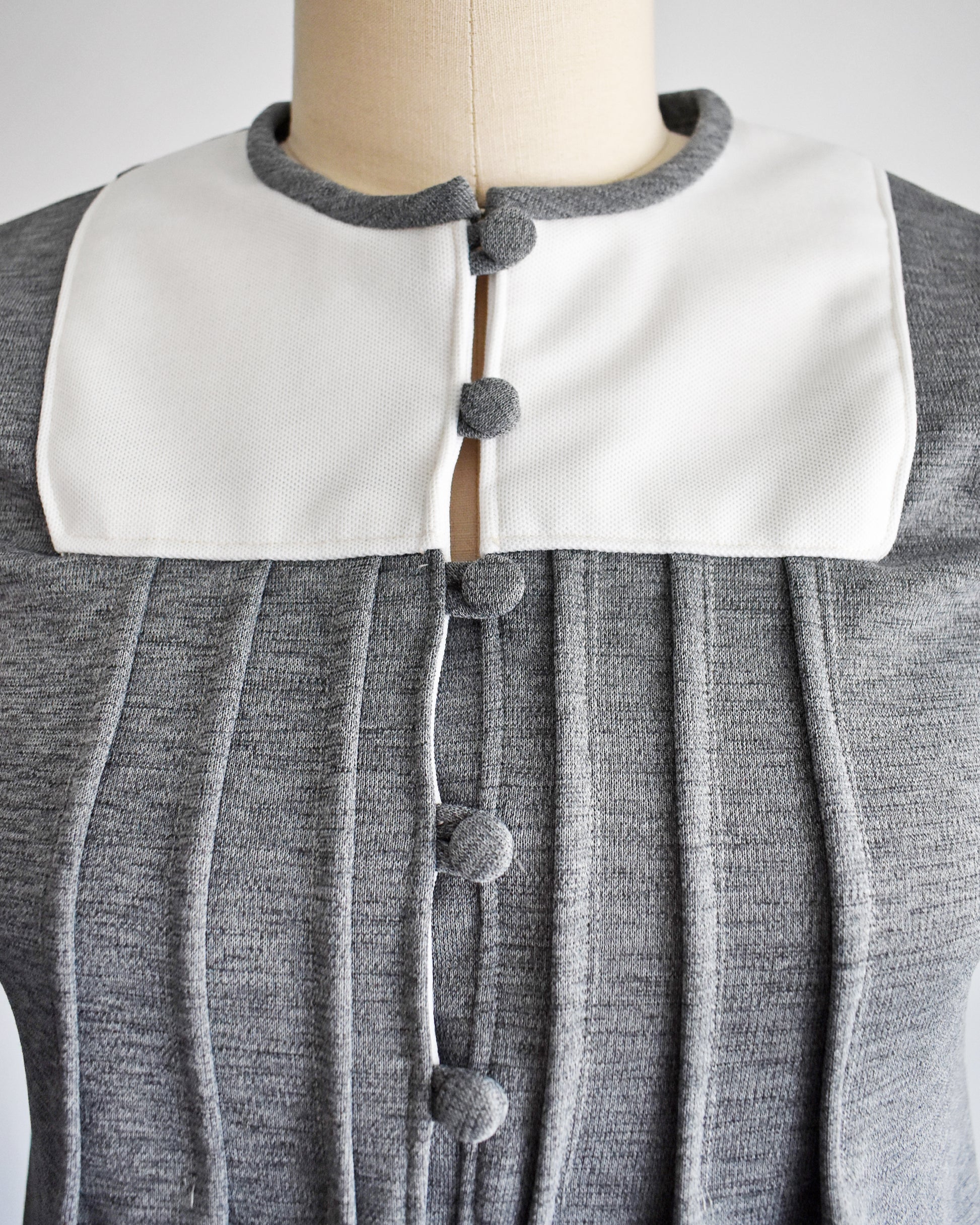close up of the bib collar area and button front on a vintage 1960s gray dress with white collar on a mannequin against a white background