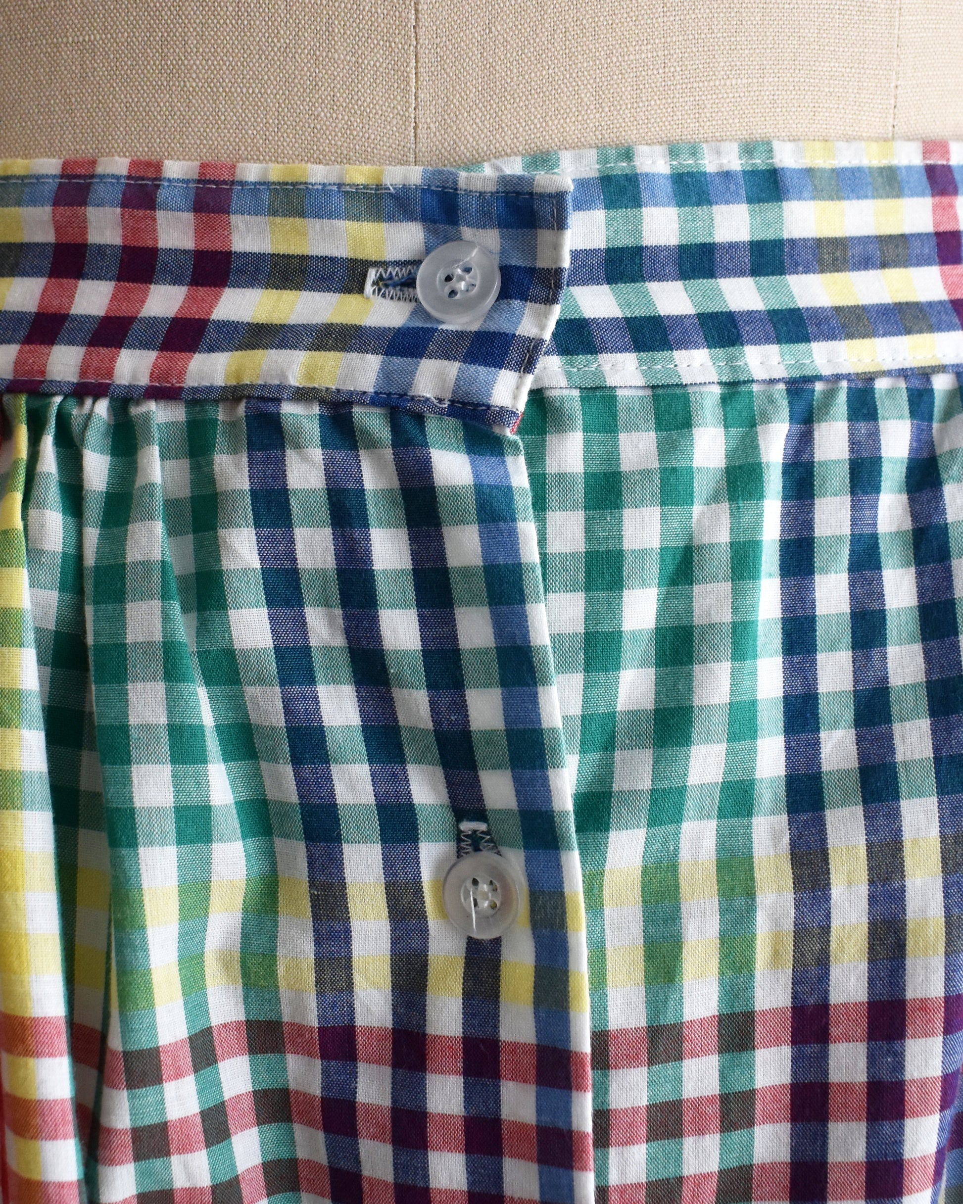 close up of the waistband on a vintage 1980s multicolor plaid midi skirt displayed on a beige dress form mannequin against a plain white background.