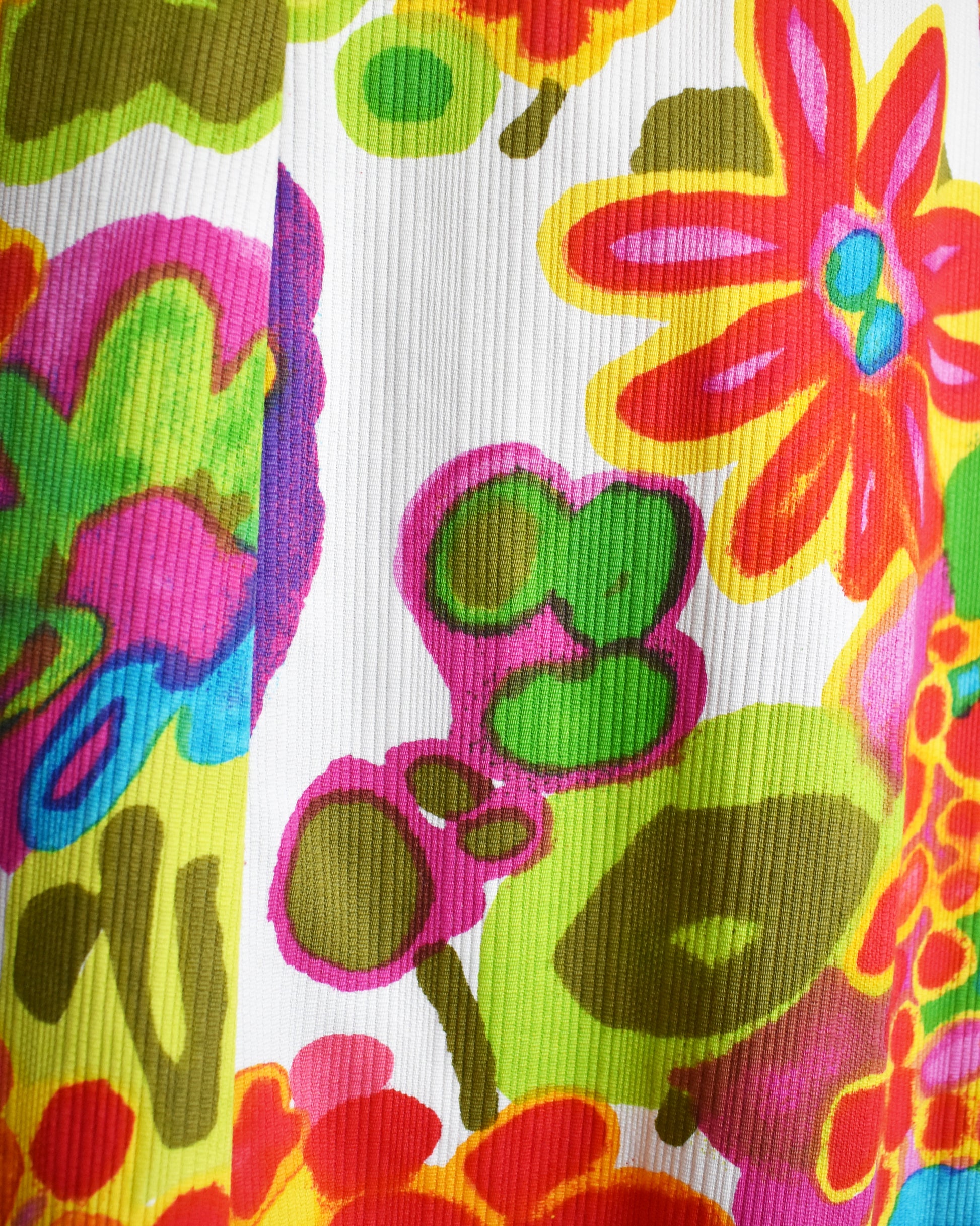 A close-up the vintage 1960s dress showing the white ribbed fabric with a vibrant, multicolor retro floral and abstract pattern in pink, green, yellow, orange, and blue.
