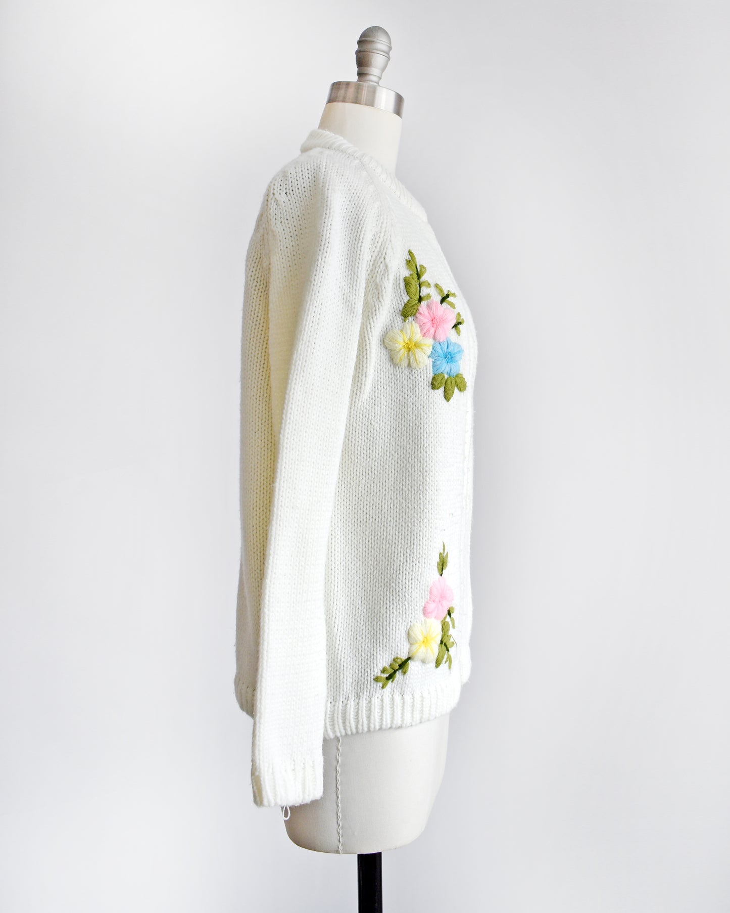 side view of a vintage 1970s white cardigan with colorful floral embroidery on the front on a dress form