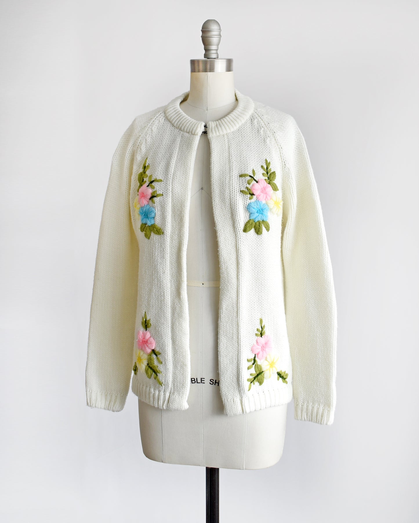 side front view of a vintage 1970s white cardigan with colorful floral embroidery on the front on a dress form