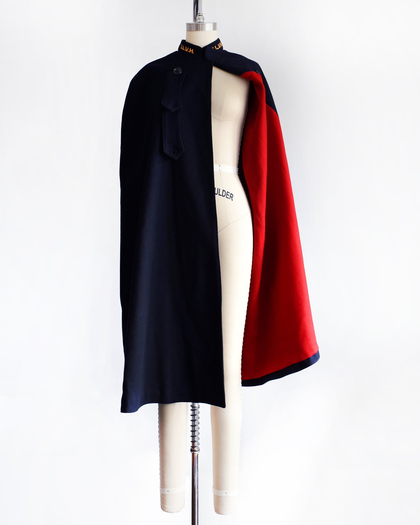 a vintage 1940s navy nurse's cape on a  mannequin against a white background. the cape is half open, showing the bright red wool lining