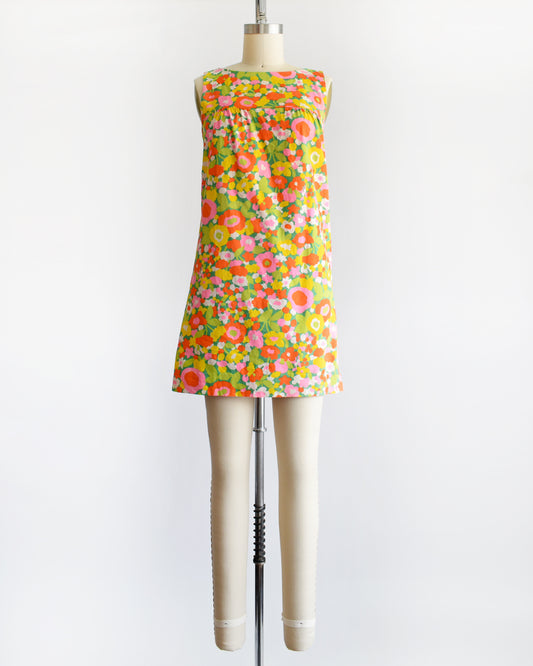 a vintage 1960s sleeveless A-line dress with a vibrant multicolor floral print, displayed on a cream-colored dress form mannequin against a plain white background.