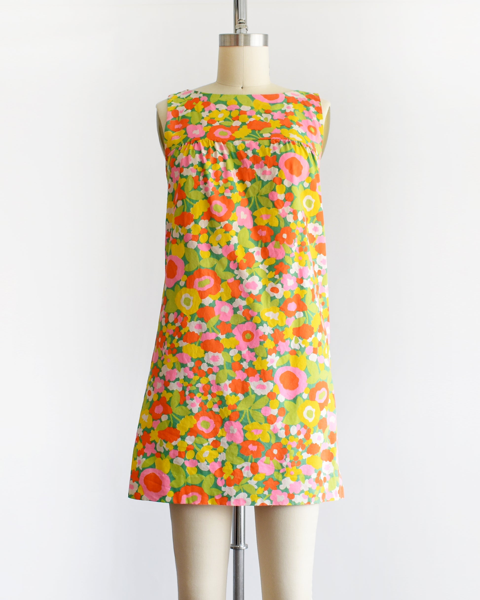 a vintage 1960s sleeveless A-line dress with a vibrant multicolor floral print, displayed on a cream-colored dress form mannequin against a plain white background.