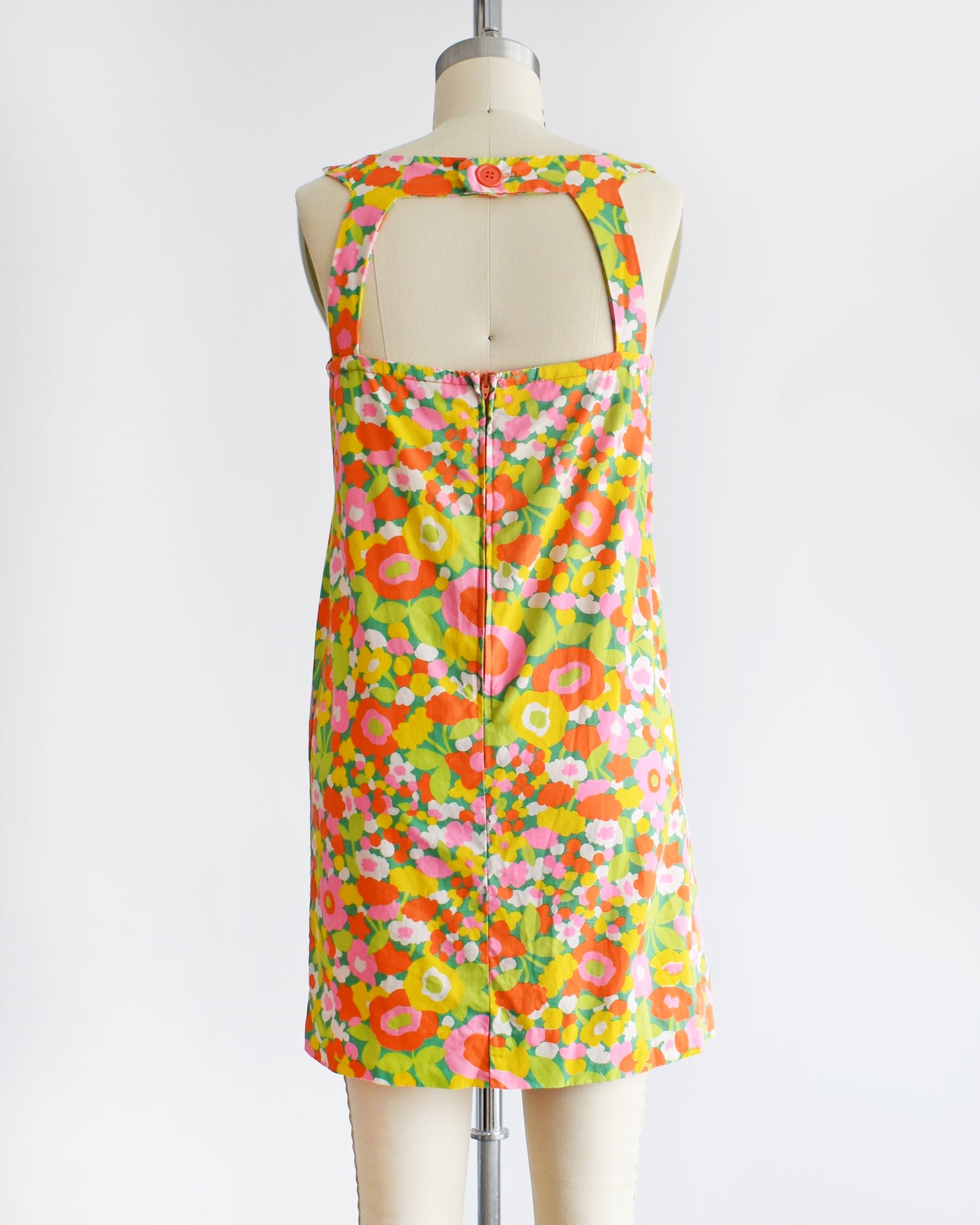 back view of a vintage 1960s sleeveless A-line dress with a vibrant multicolor floral print, displayed on a cream-colored dress form mannequin against a plain white background.