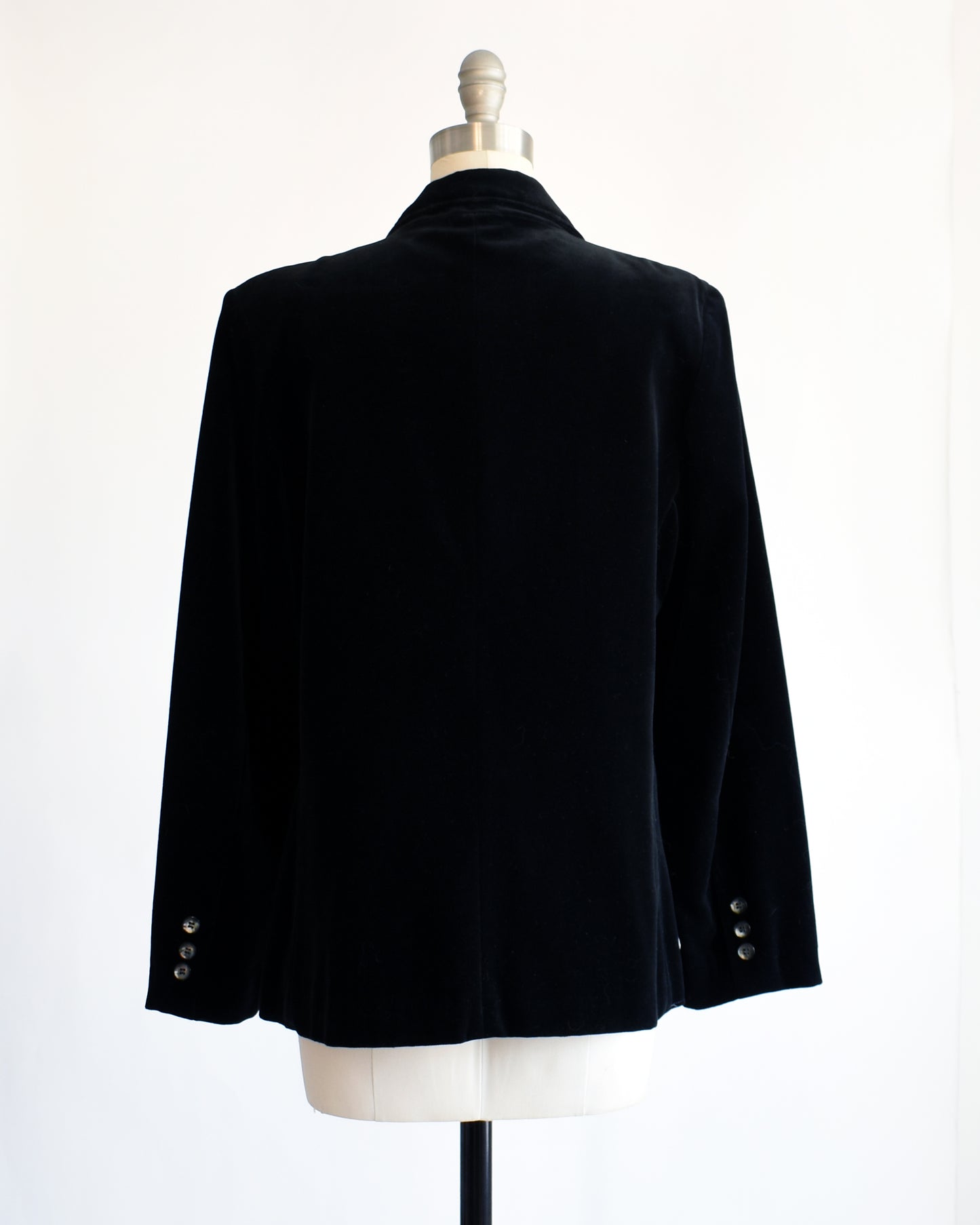 back view of a vintage 1980s black velvet  blazer on a mannequin against a white background
