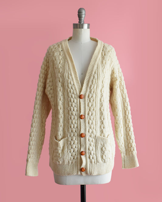 a vintage 1980s cream-colored cable knit cardigan on a mannequin against a pink background