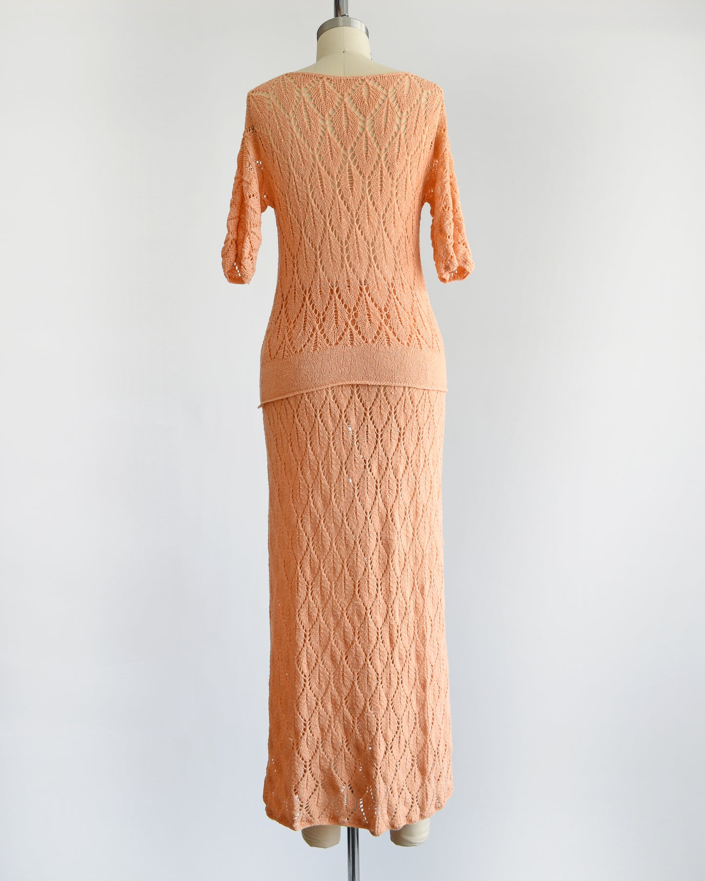 back view of a vintage 60s peach pointelle knit sweater set which includes a matching sweater and maxi skirt. The set is shown with the sweater untucked.