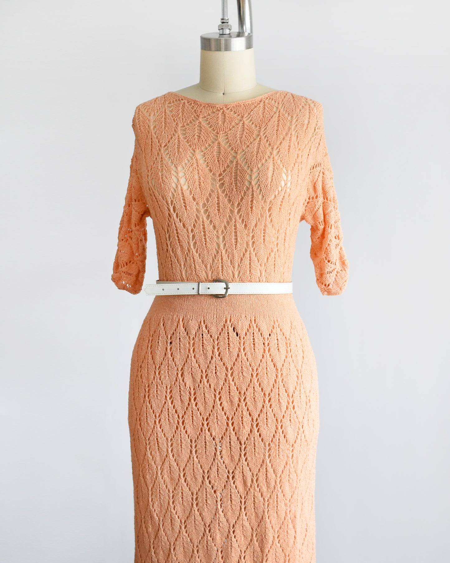 side front view of a vintage 60s peach pointelle knit sweater set which includes a matching sweater and maxi skirt. The set is shown with a white belt, which isn't included.