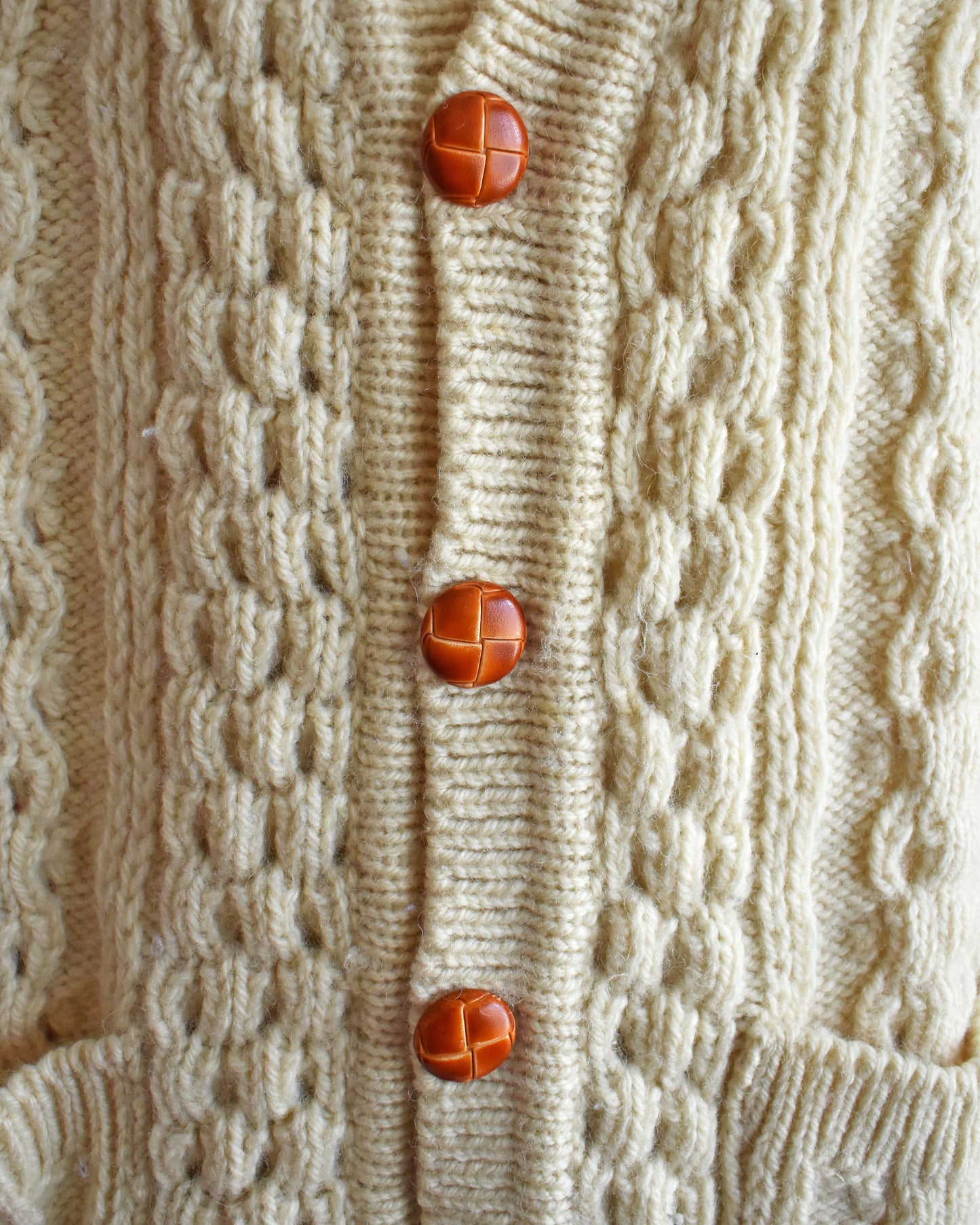 close up of the faux wood buttons on a vintage 1980s cream-colored cable knit cardigan on a mannequin against a pink background