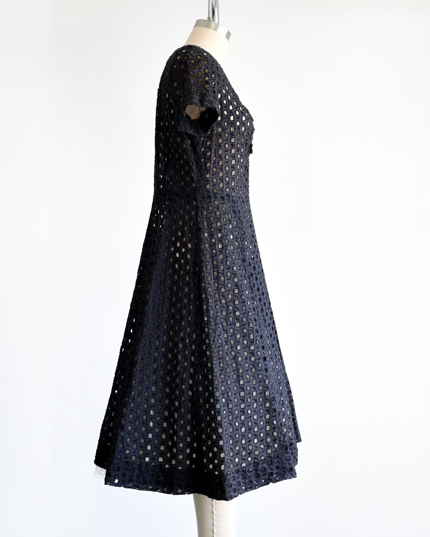 side view of a vintage 1950s black eyelet dress that has 5 rhinestone buttons under the neckline