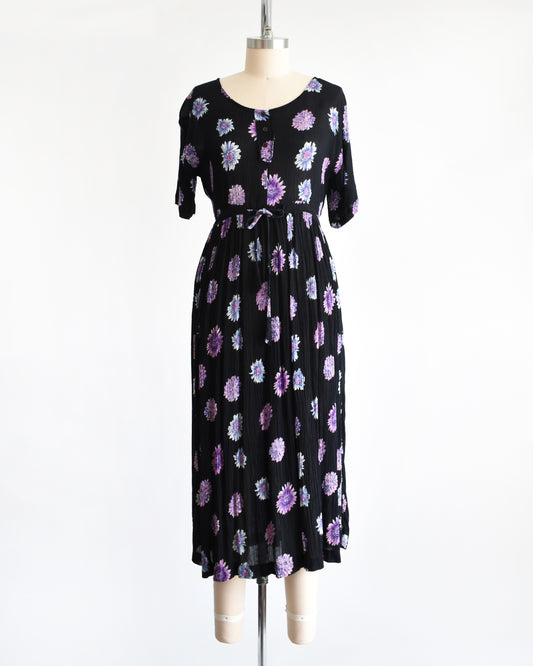 a vintage 1970s black midi dress with a purple and blue floral pattern, displayed on a mannequin against a plain white background.