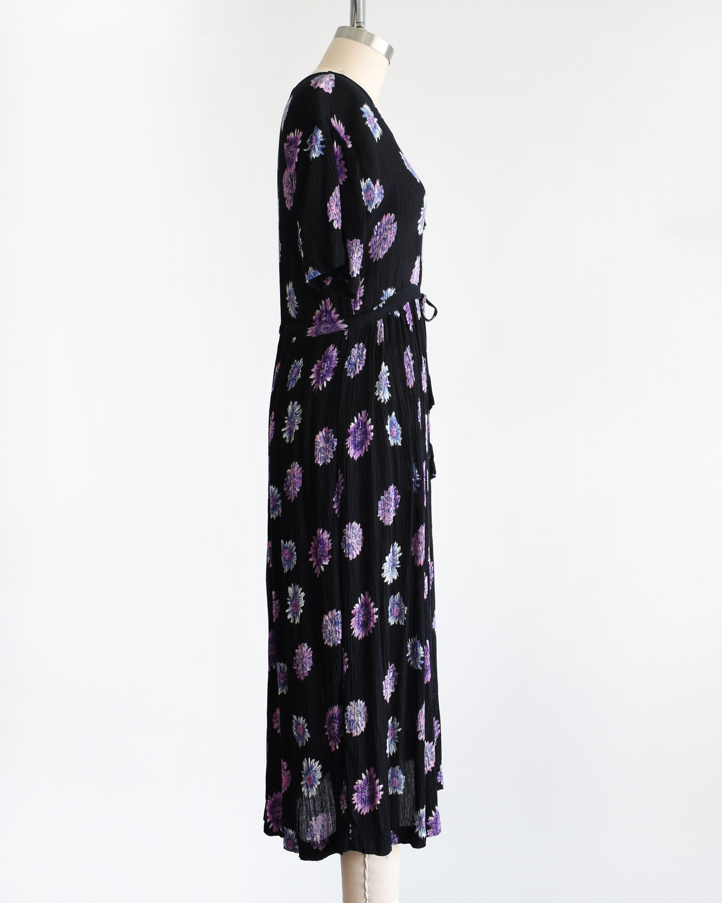 side view of a vintage 1970s black midi dress with a purple and blue floral pattern, displayed on a mannequin against a plain white background.