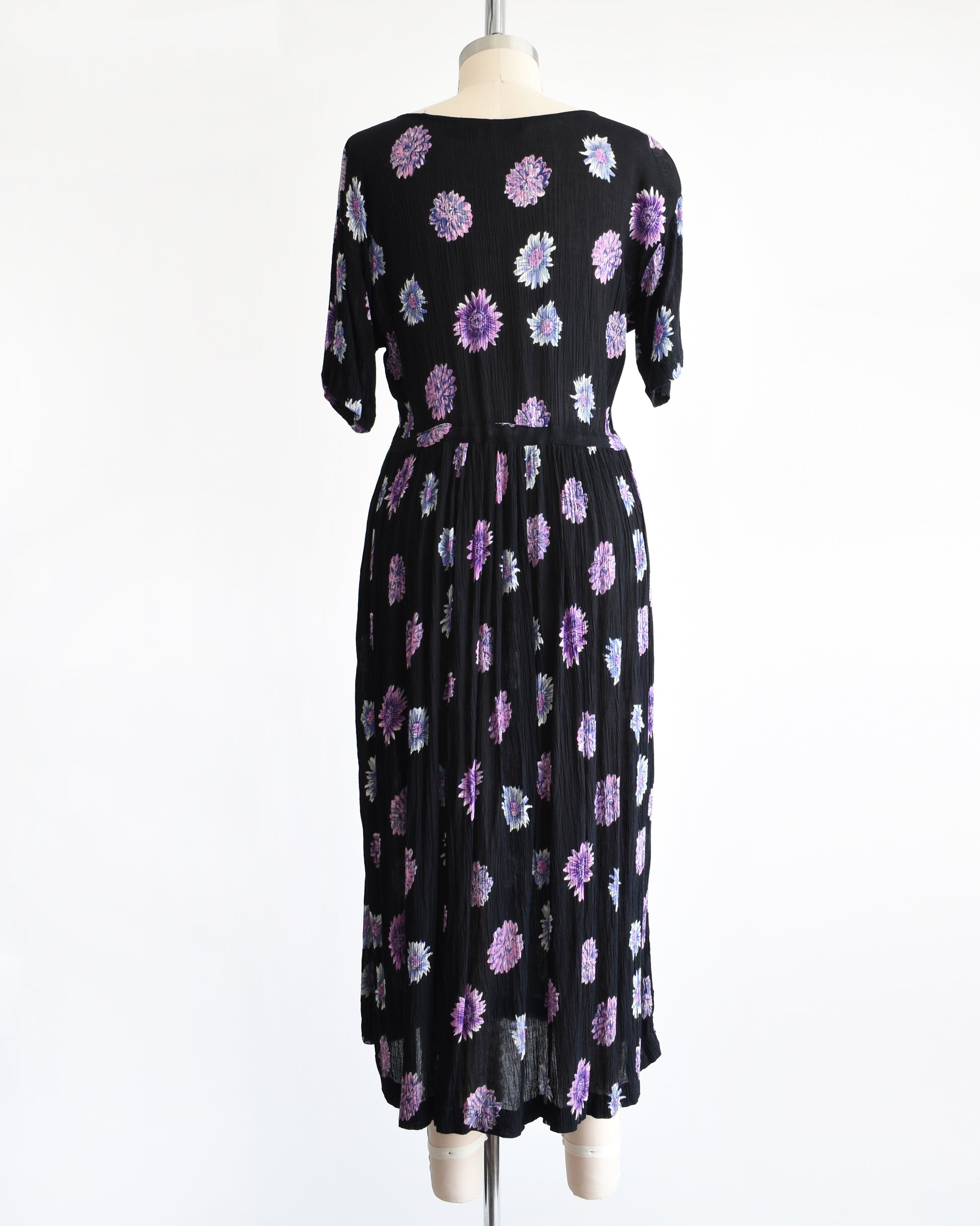 back view of a vintage 1970s black midi dress with a purple and blue floral pattern, displayed on a mannequin against a plain white background.