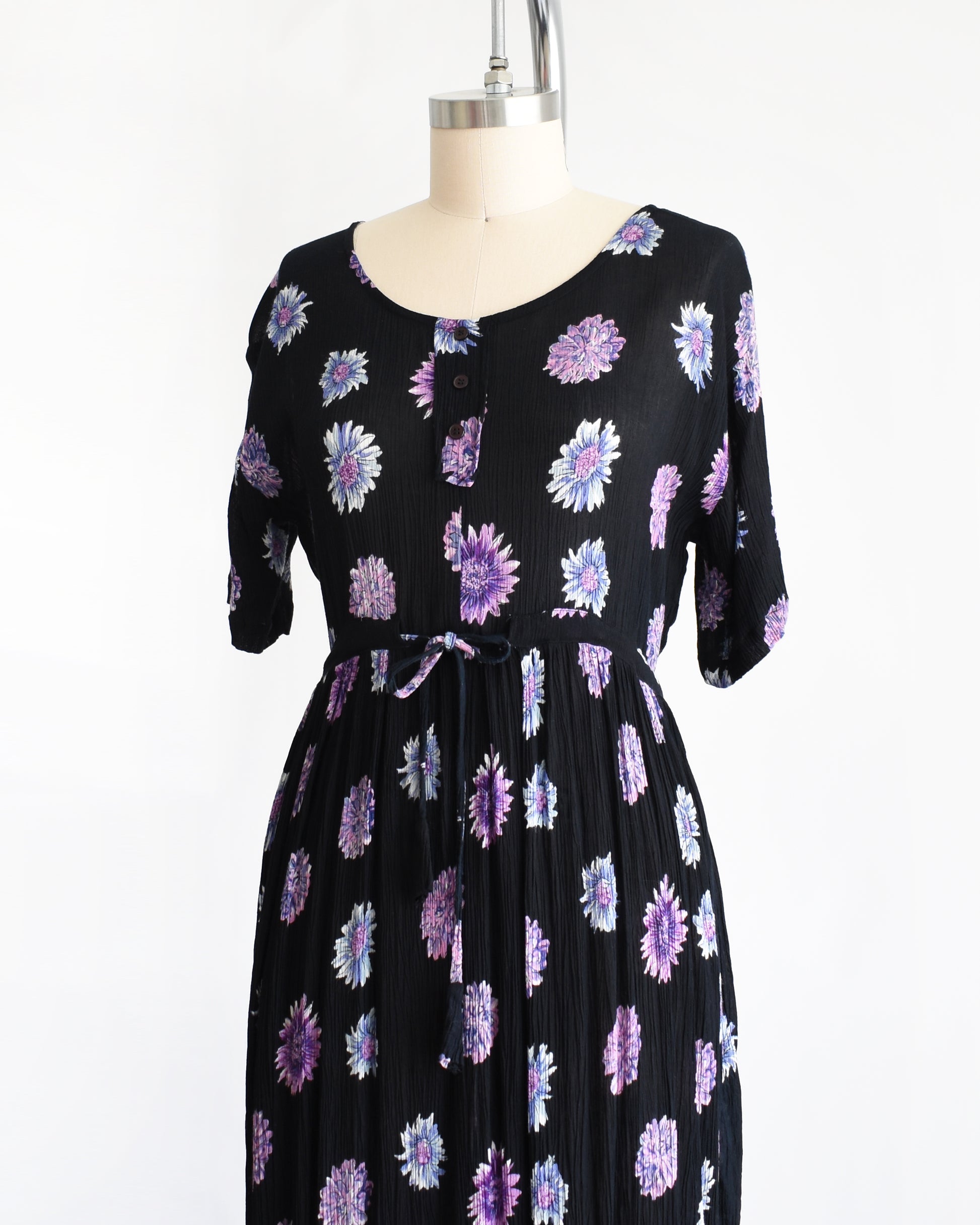 side front view of a vintage 1970s black midi dress with a purple and blue floral pattern, displayed on a mannequin against a plain white background.