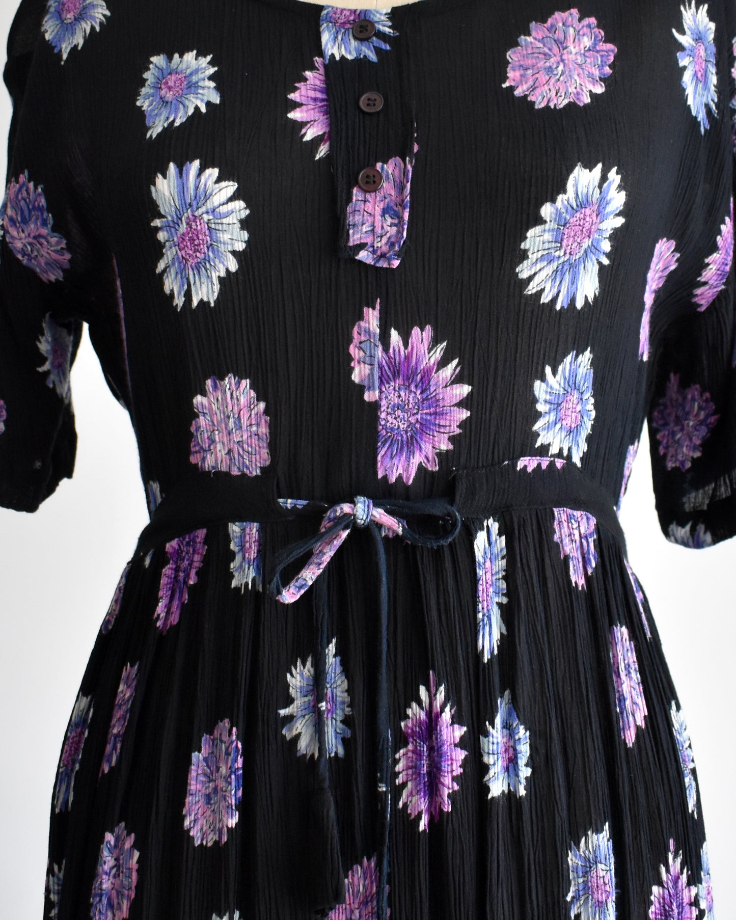 close up of the waist on a vintage 1970s black midi dress with a purple and blue floral pattern, displayed on a mannequin against a plain white background.