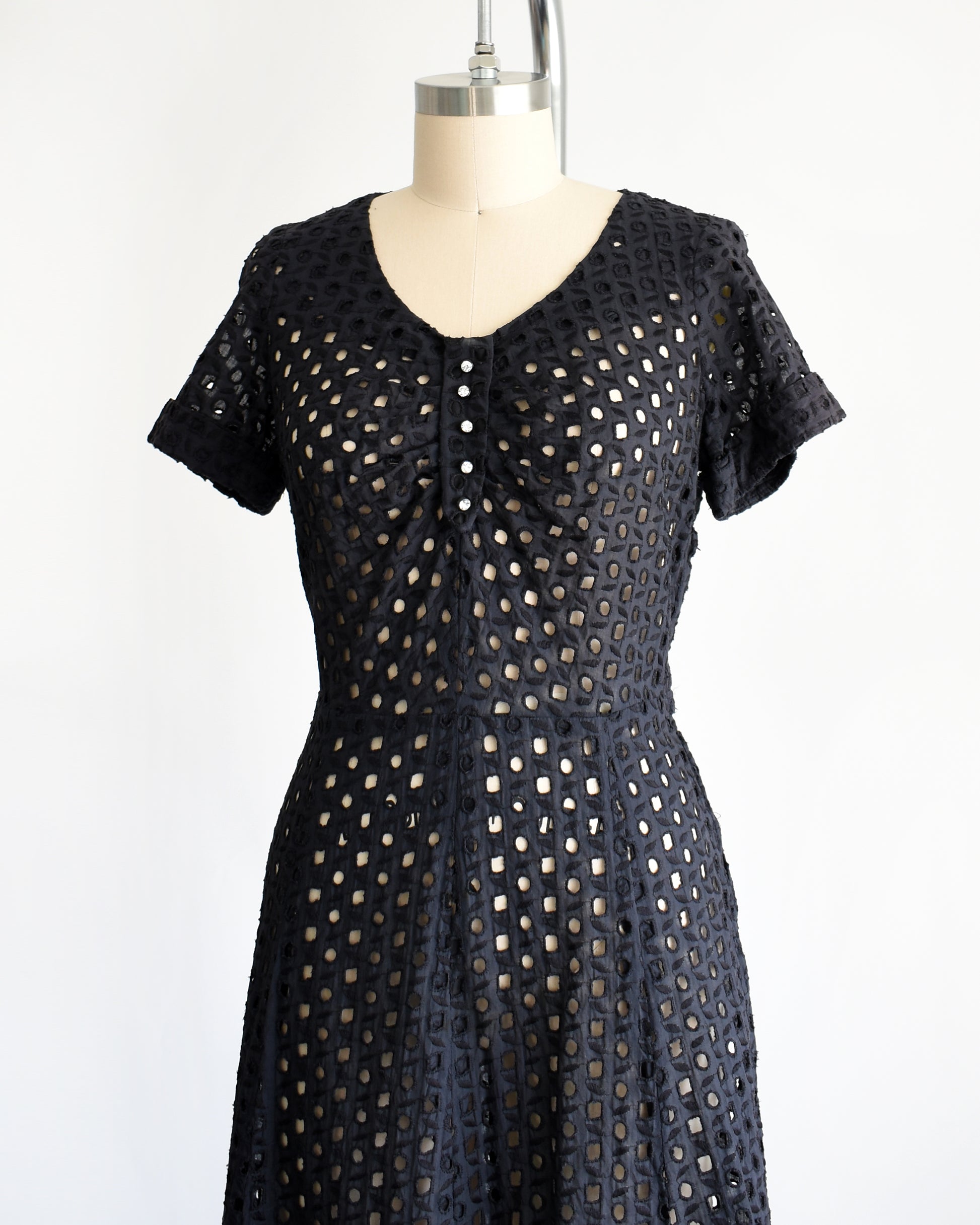 side front view of a vintage 1950s black eyelet dress that has 5 rhinestone buttons under the neckline