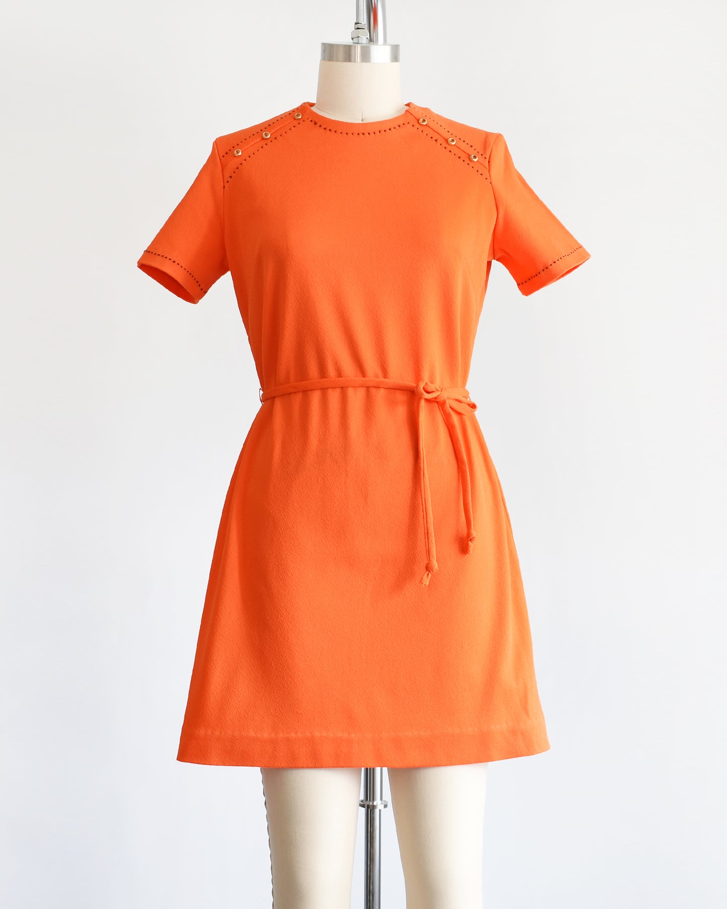 a vintage 1960s orange mod dress with black stitch trim on the front collar and shoulders, along with decorative gold buttons on the shoulder.