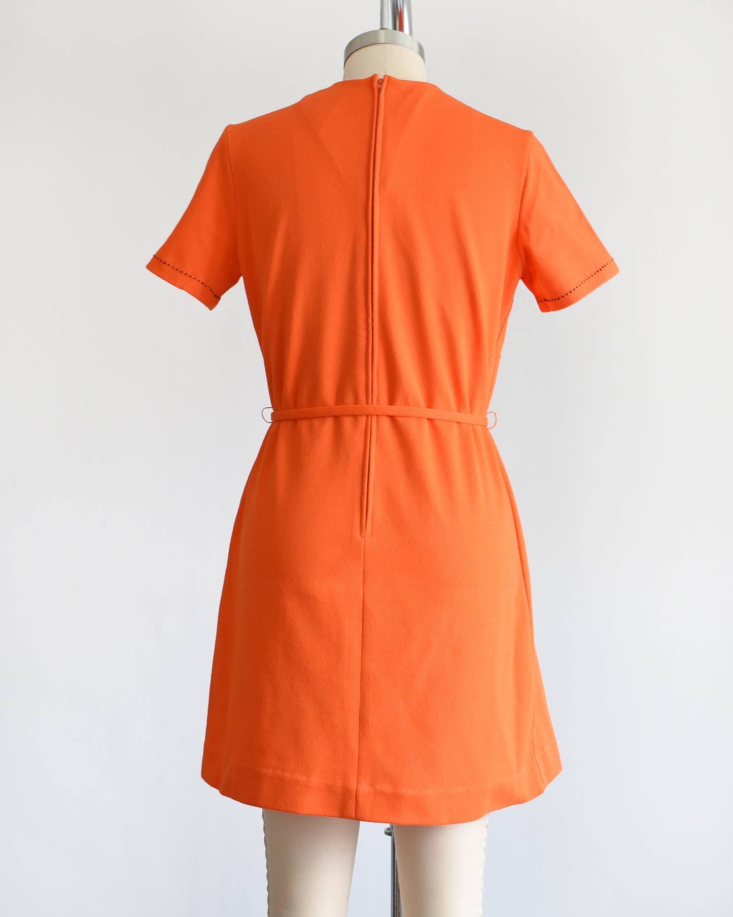 back view of a vintage 1960s orange mod dress with black stitch trim on the front collar and shoulders, along with decorative gold buttons on the shoulder.