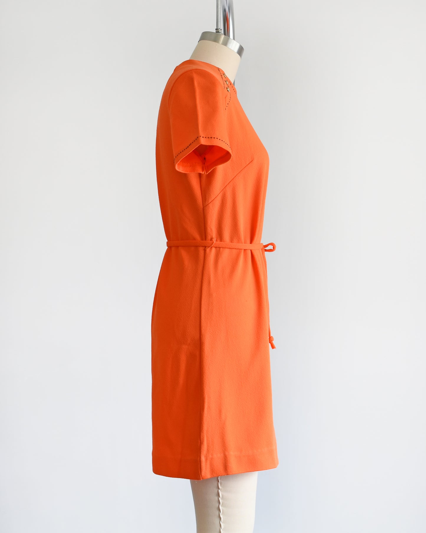 side view of a vintage 1960s orange mod dress with black stitch trim on the front collar and shoulders, along with decorative gold buttons on the shoulder.