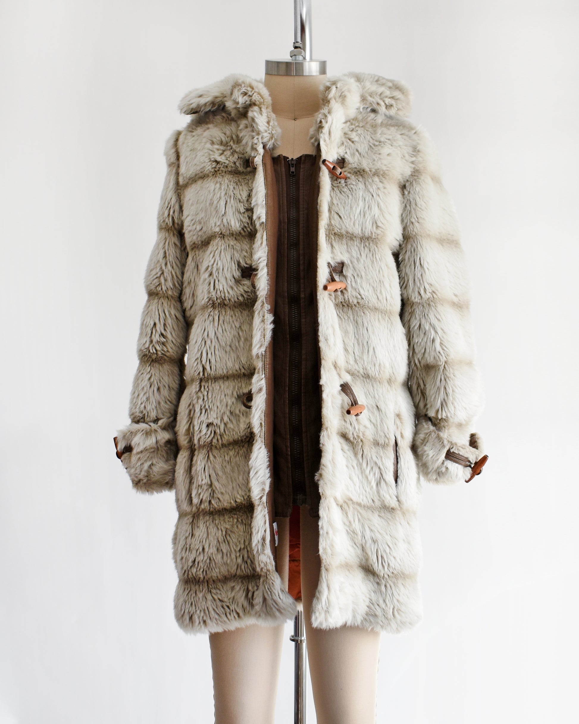 a vintage 1970s faux fur coat with hood on a mannequin against a white background. the coat is unbuttoned showing the inside zipper