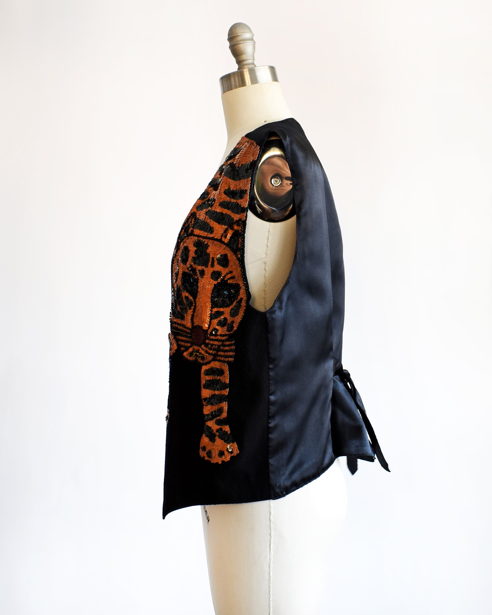 side view of a vintage 1980s black vest with an orange sequin tiger on a mannequin against a white background