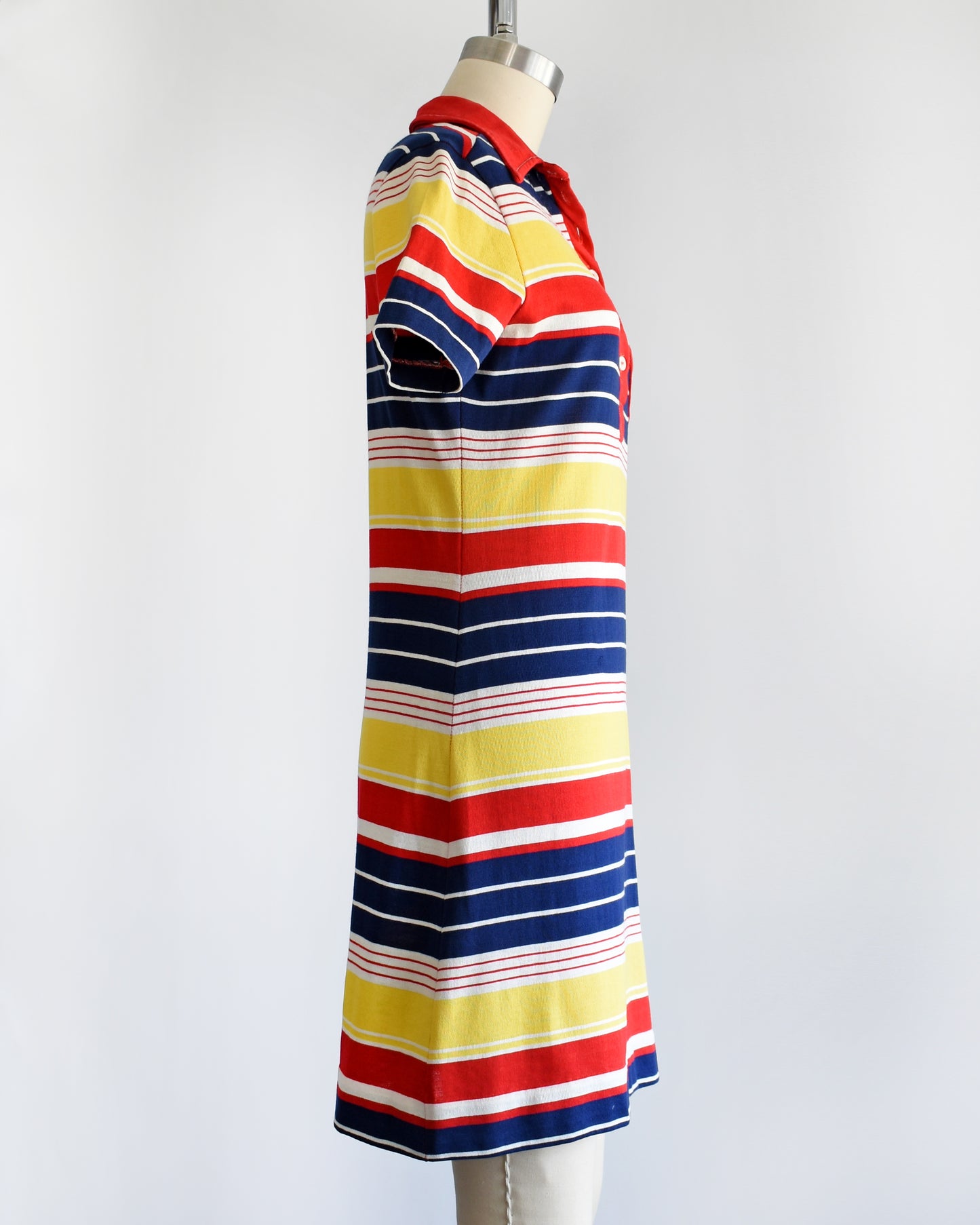 side view of a vintage 1970s red, navy blue, yellow, and white striped dress with a red collar with six buttons down the front and a matching red chest pocket.