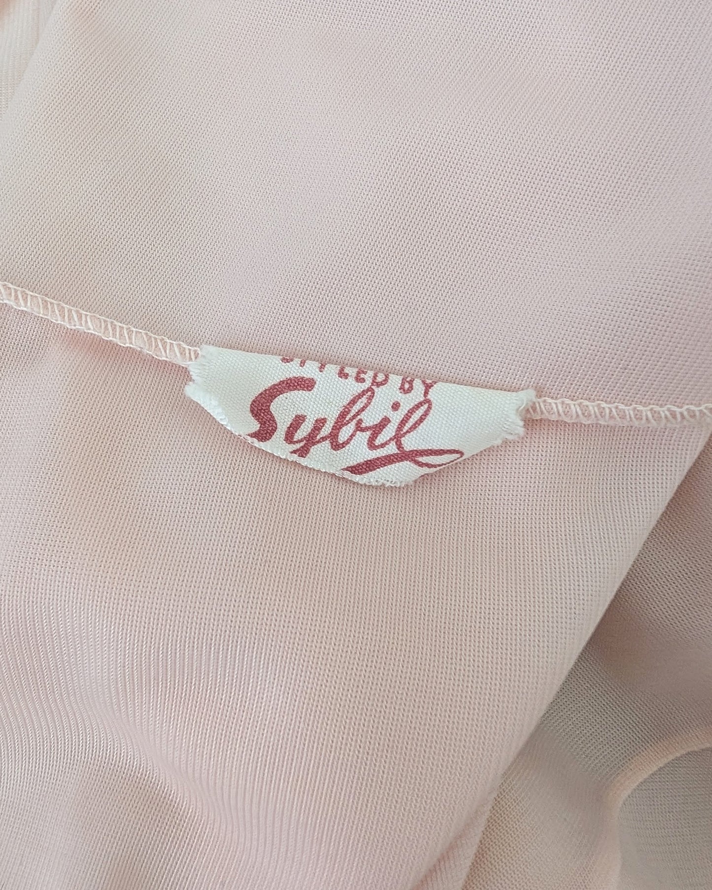 Close-up of a small white sewn label reading 'Styled by Sybil' in red script.
