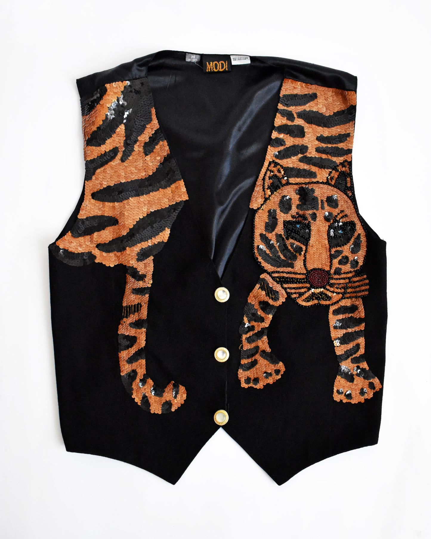 overhead shot of a vintage 1980s black vest with an orange sequin tiger on a white background