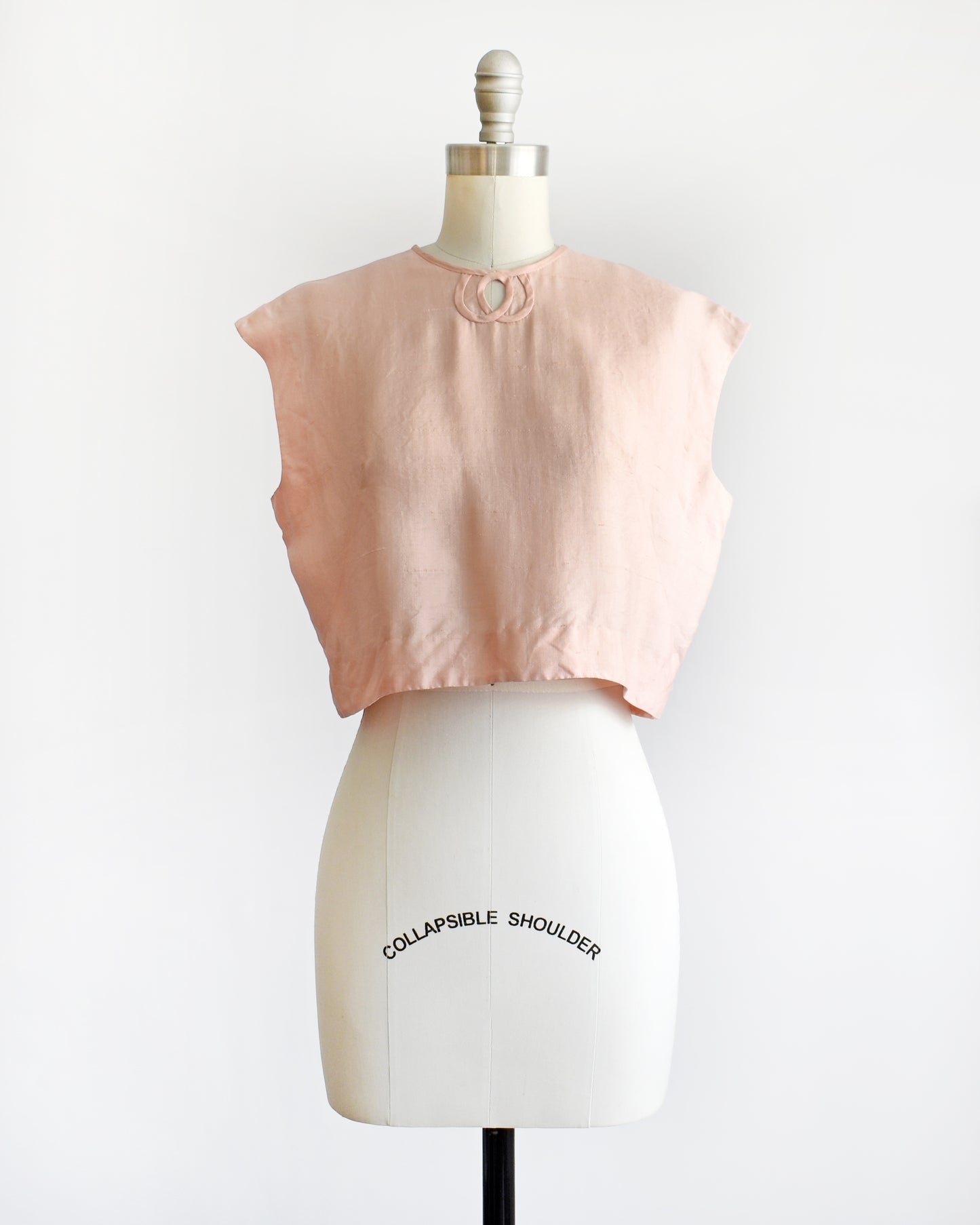 a vintage 1950s/1960s pale pink sleeveless silk crop top displayed on a white dress form mannequin against a plain white background. 