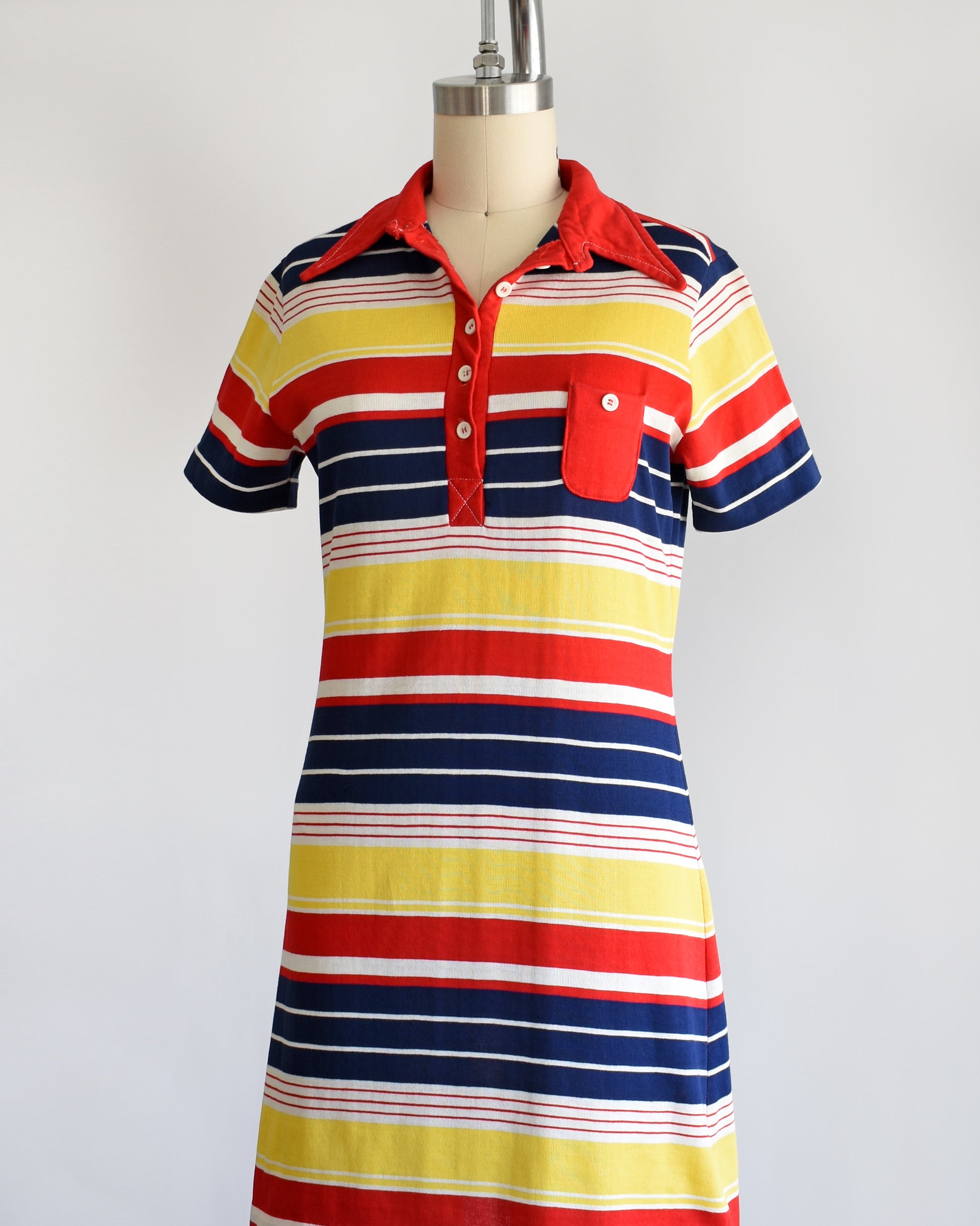 side front view of a vintage 1970s red, navy blue, yellow, and white striped dress with a red collar with six buttons down the front and a matching red chest pocket.