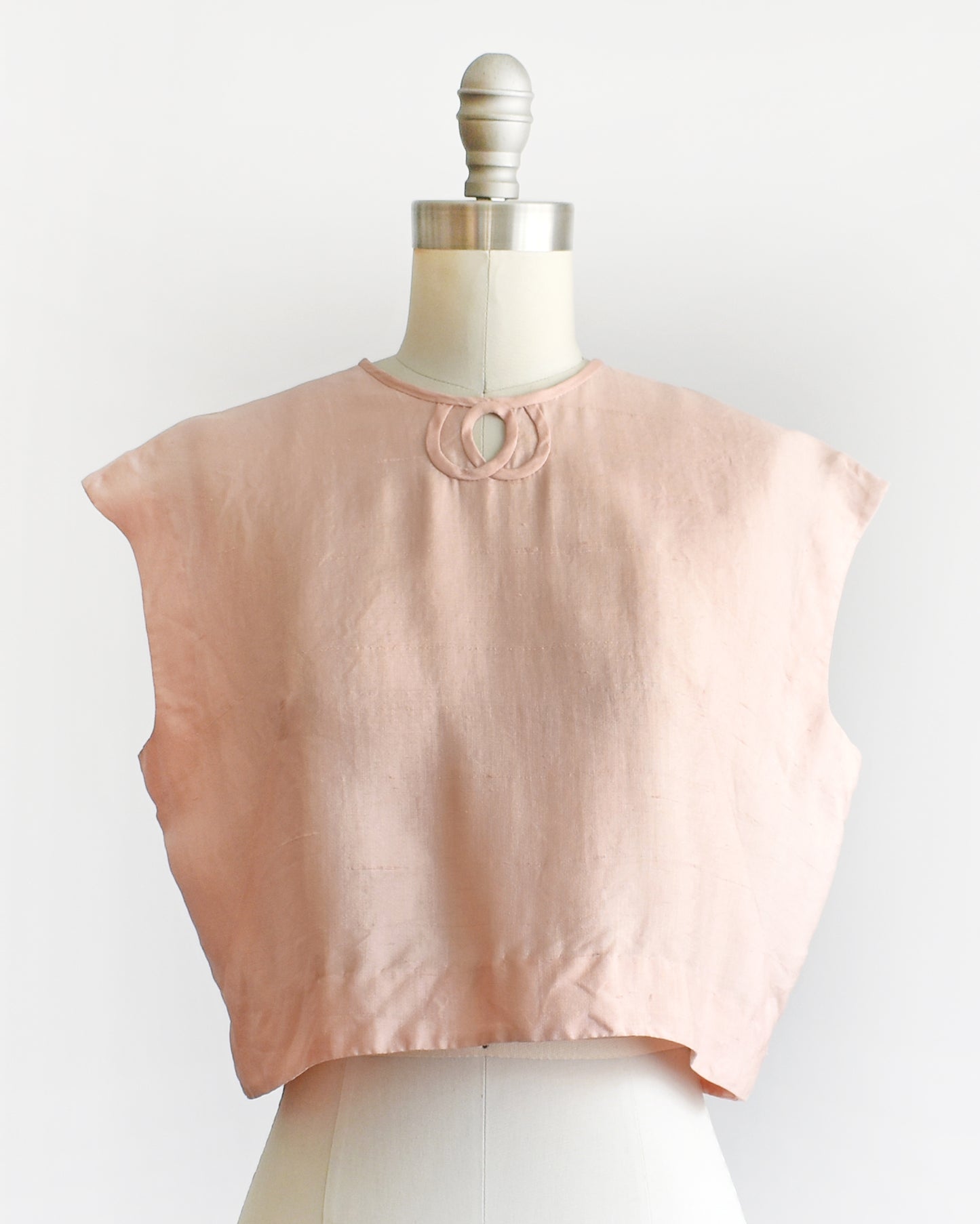 a vintage 1950s/1960s pale pink sleeveless silk crop top displayed on a white dress form mannequin against a plain white background. 