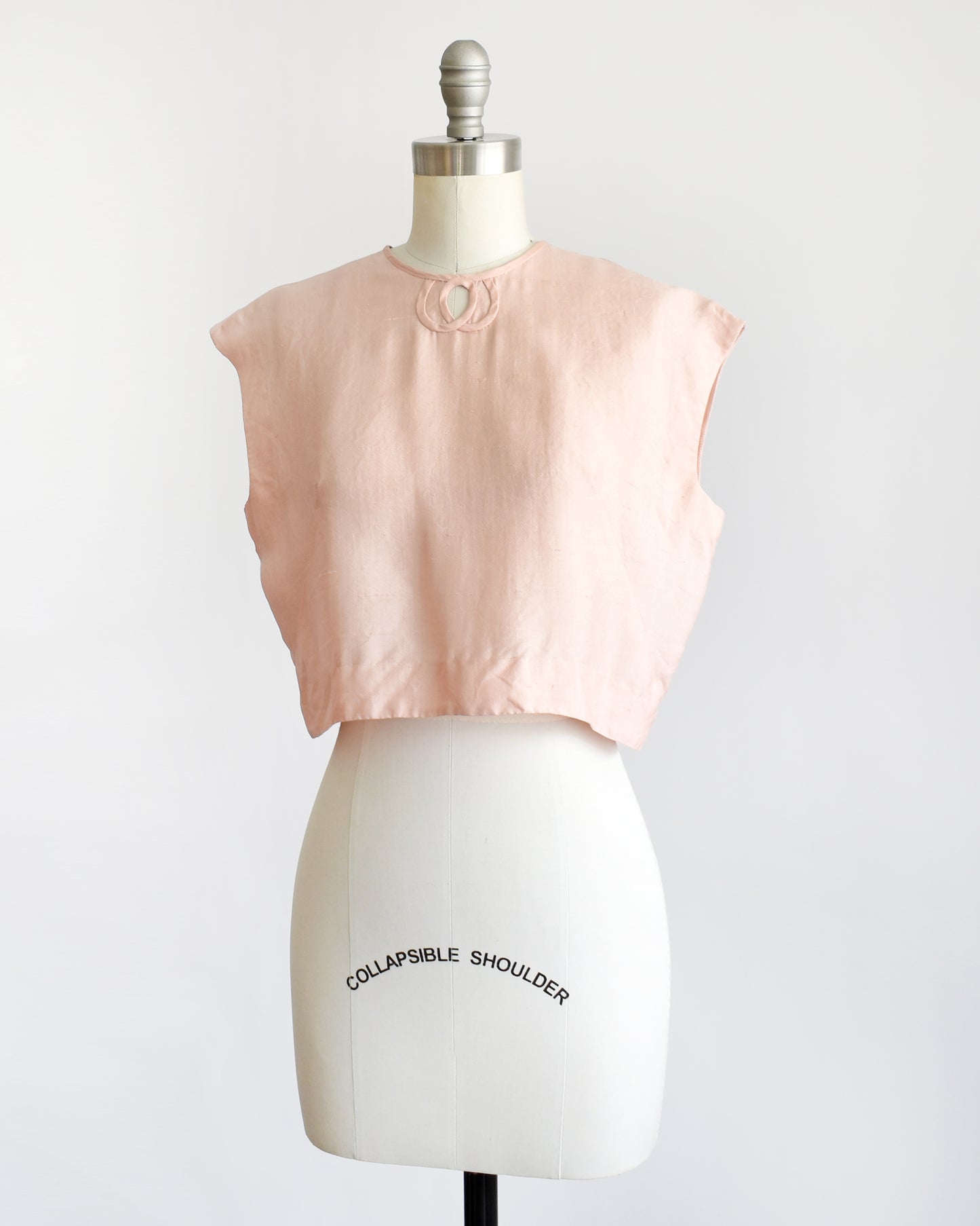 side view of a vintage 1950s/1960s pale pink sleeveless silk crop top displayed on a white dress form mannequin against a plain white background. 