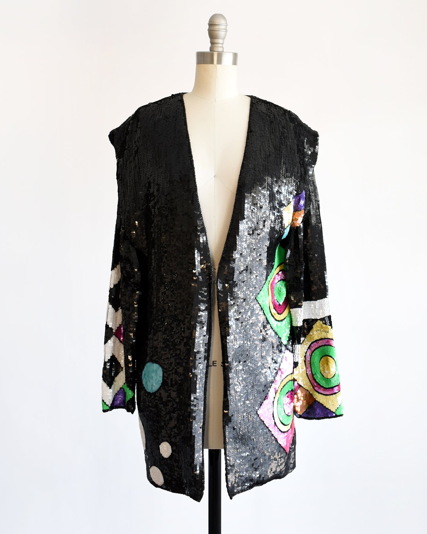 a vintage 1980s 1990s black sequin cardigan jacket with colorful abstract patterns on a mannequin against a white background