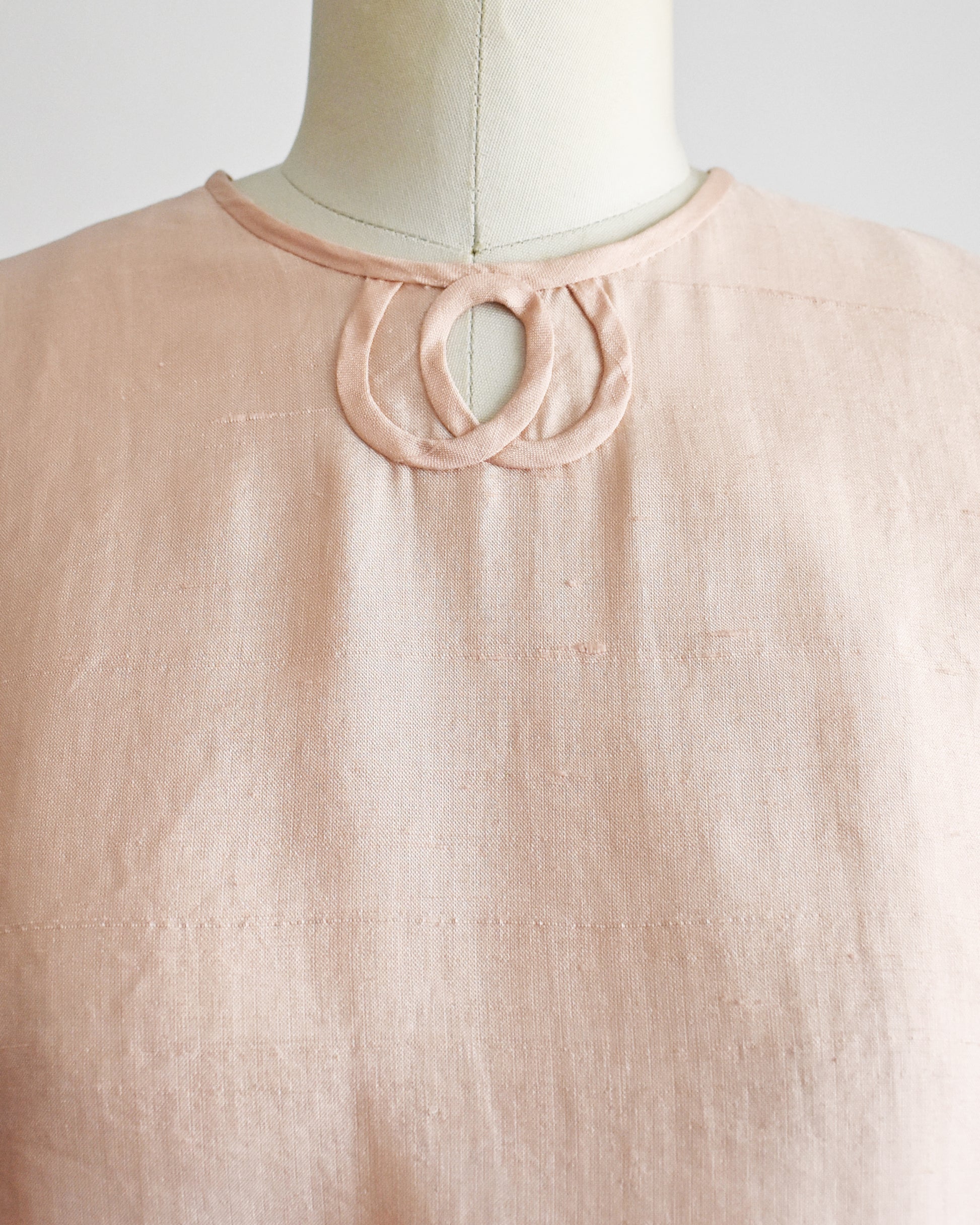 close up of the keyhole neckline on a vintage 1950s/1960s pale pink sleeveless silk crop top displayed on a white dress form mannequin against a plain white background. 